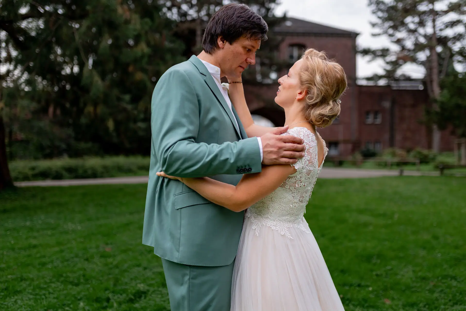 Bräutigam hält die Hände der strahlenden Braut im Spitzenkleid, historisches Schlossgebäude im Hintergrund