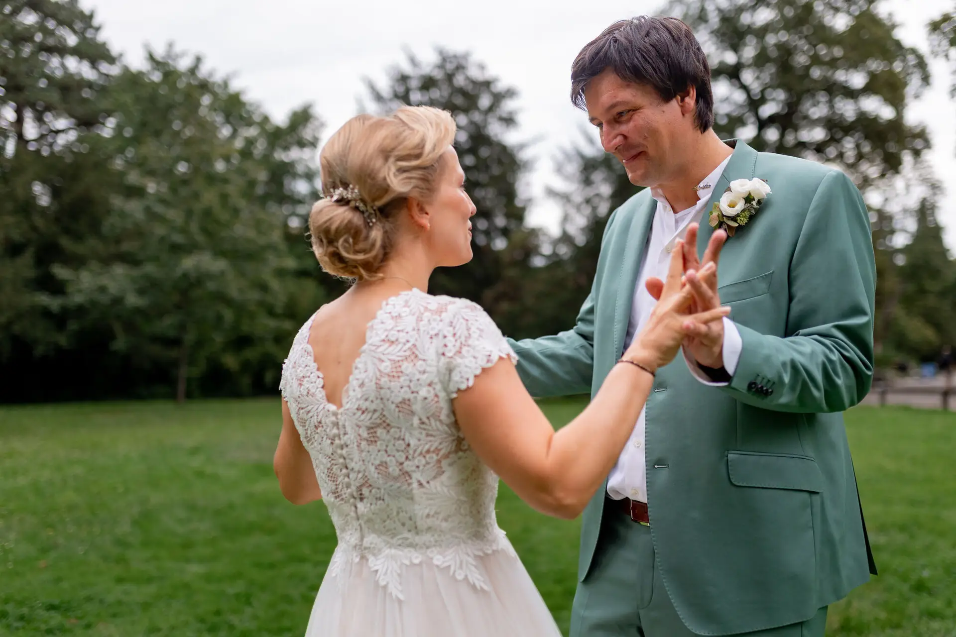 Brautpaar tanzt ausgelassen auf grüner Wiese im Schlossgarten, umgeben von alten Bäumen