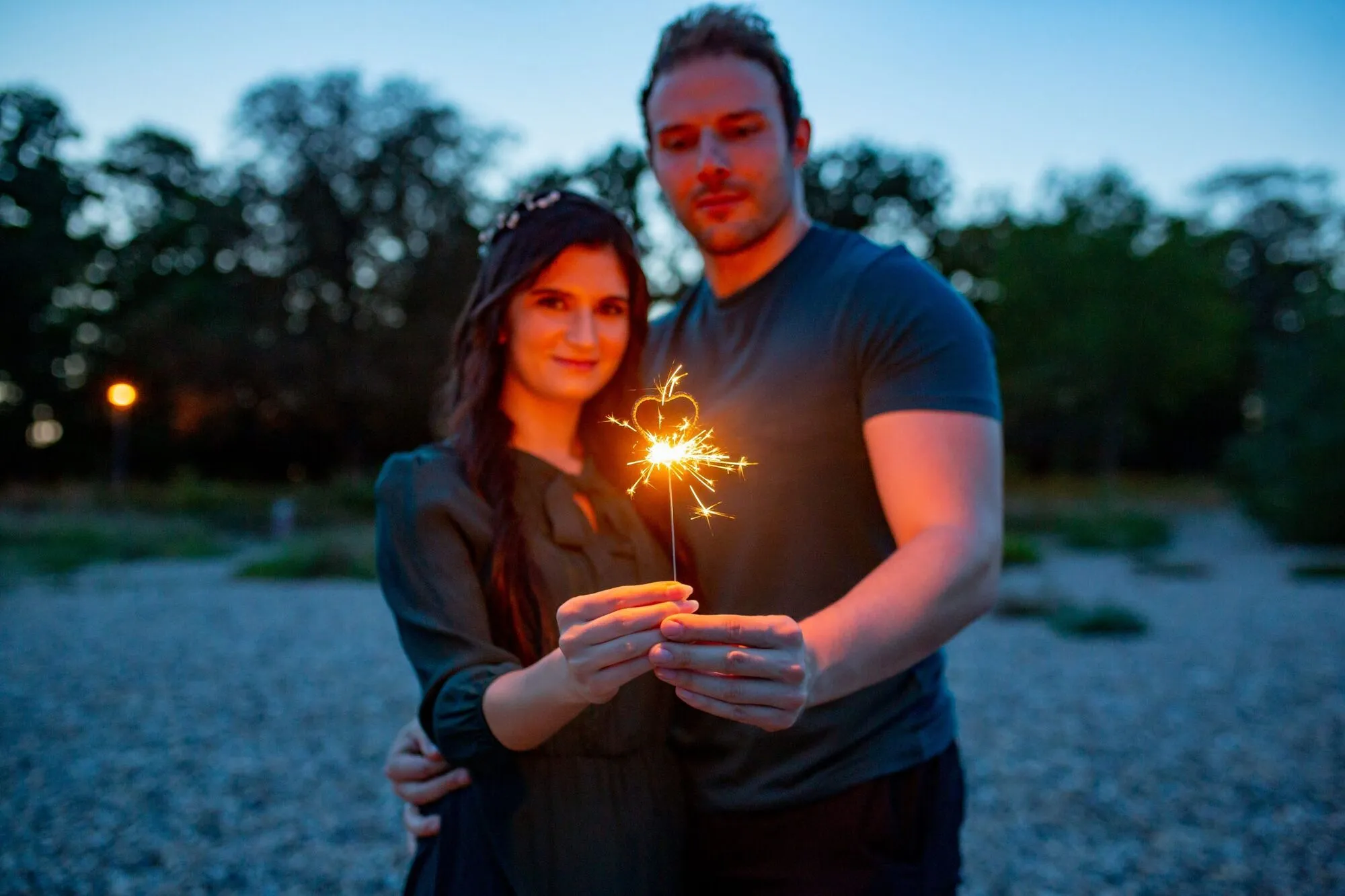 Davina und Keven halten gemeinsam eine Wunderkerze in der blauen Stunde auf der Parkinsel Ludwigshafen