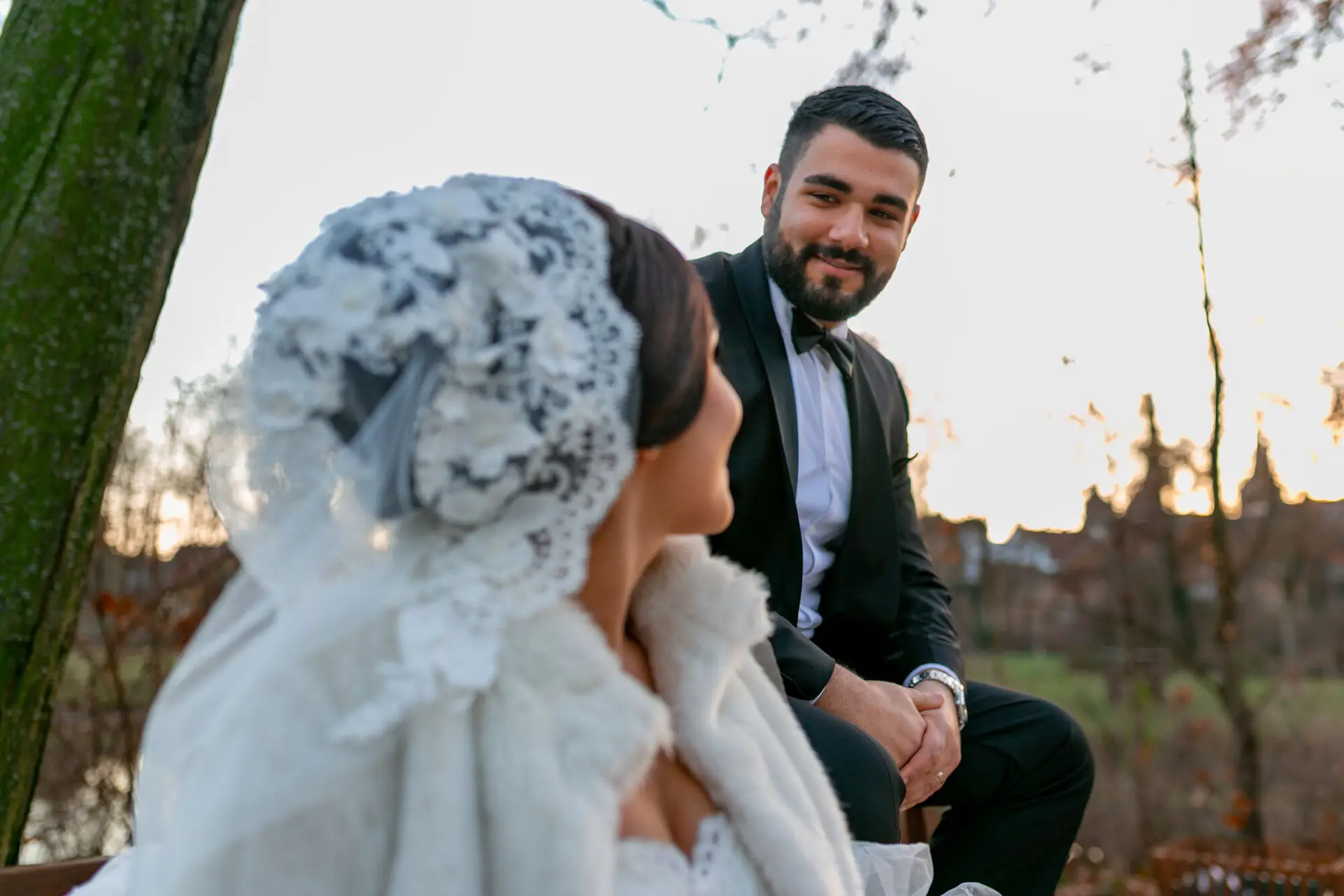 Bräutigam betrachtet Braut mit Spitzenschleier zärtlich, Nahaufnahme auf Parkbank im winterlichen Schlossgarten