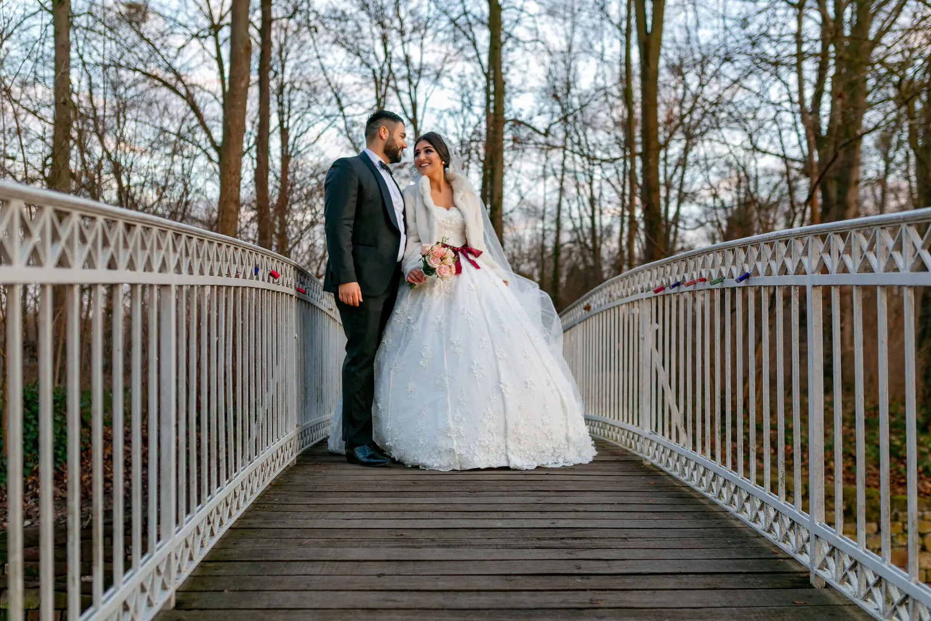 Brautpaar auf der Brücke mit weißem Geländer im winterlichen Schlossgarten, kahle Bäume als natürlicher Rahmen