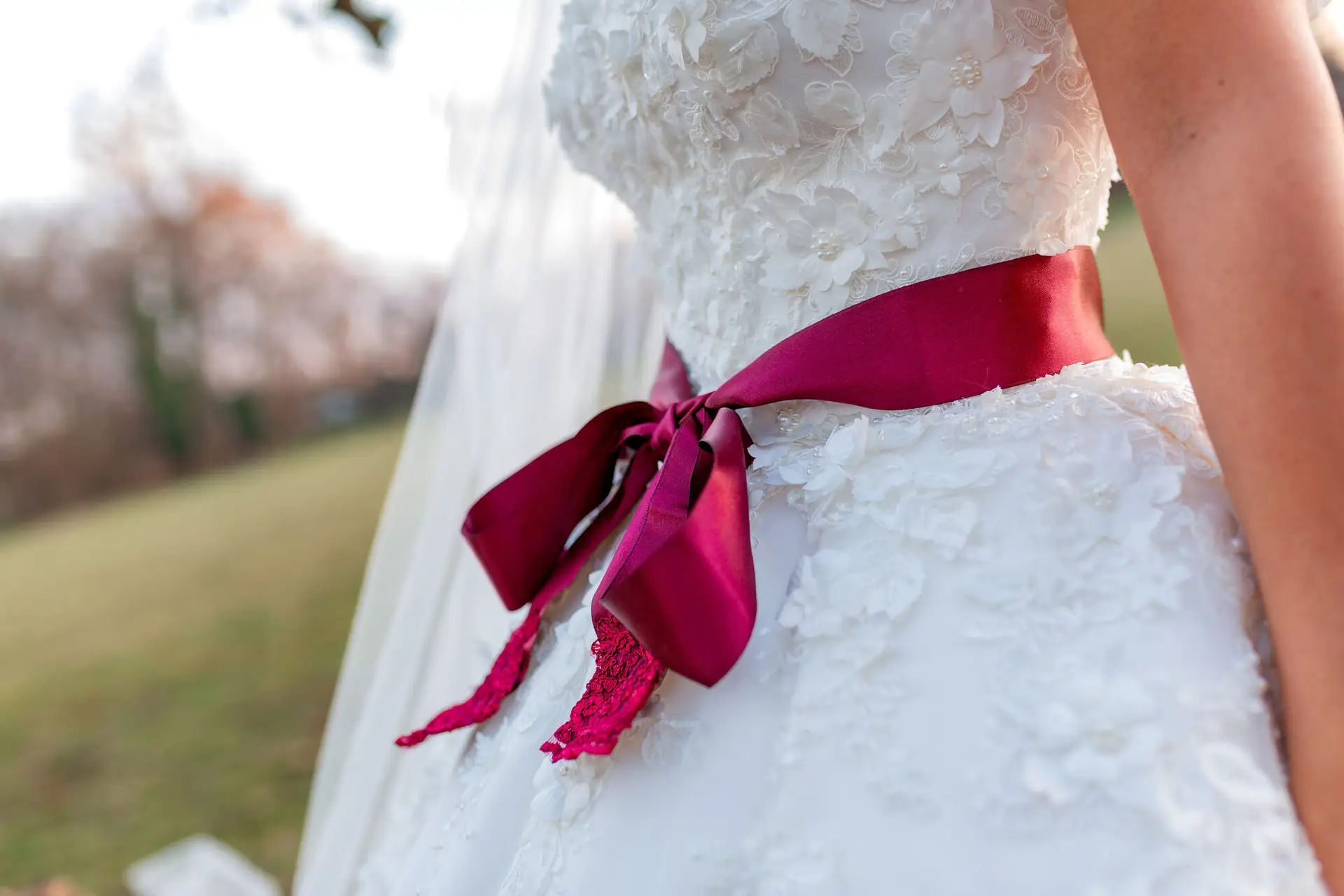 Nahaufnahme des Hochzeitskleides mit floraler Spitze und magentafarbener Satinschleife