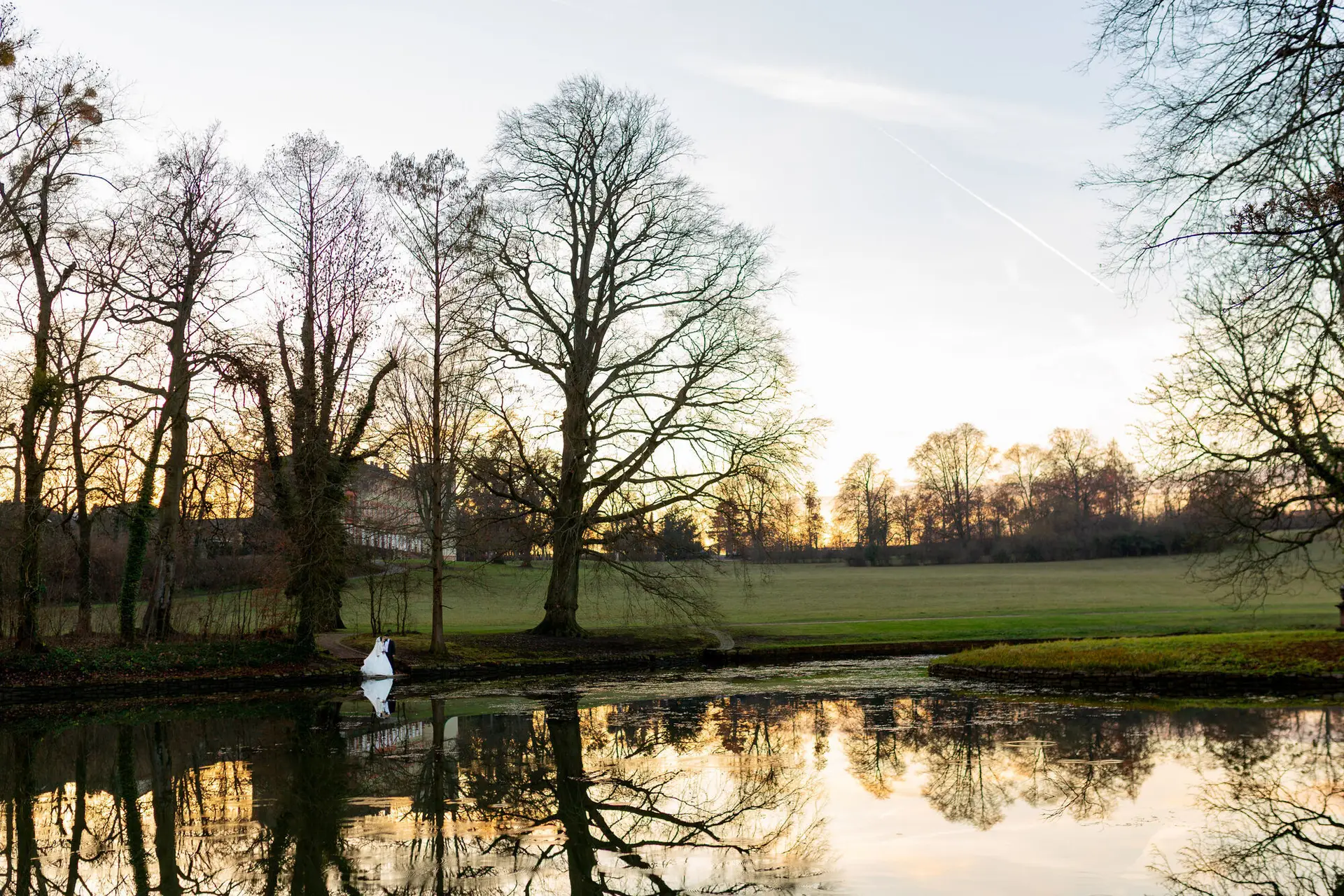 Winterliche Landschaft am Schlossteich bei Sonnenuntergang, kahle Bäume spiegeln sich im Wasser