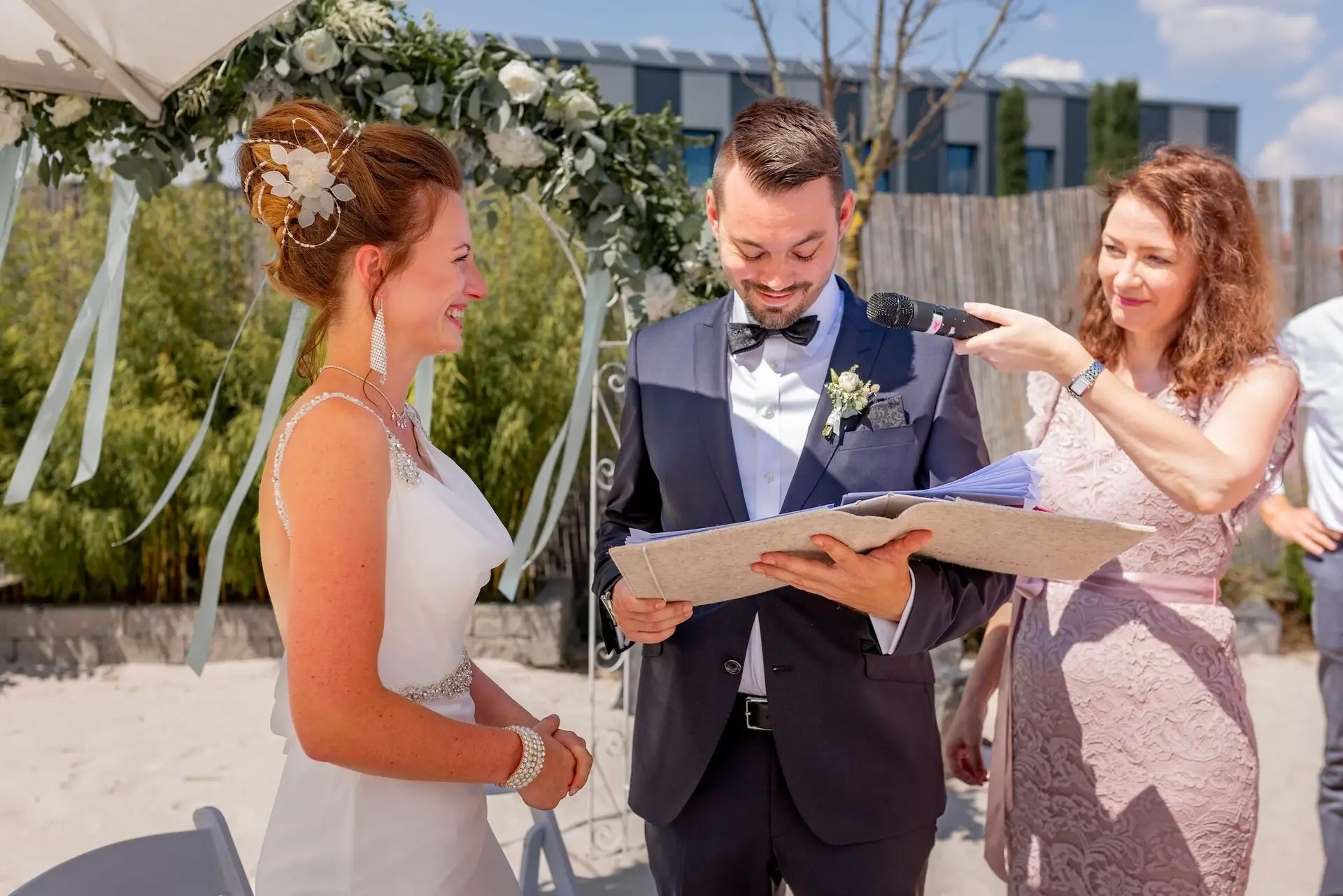 Brautpaar vor dem Blumenaltar während die Traurednerin den Text der freien Trauung vorliest