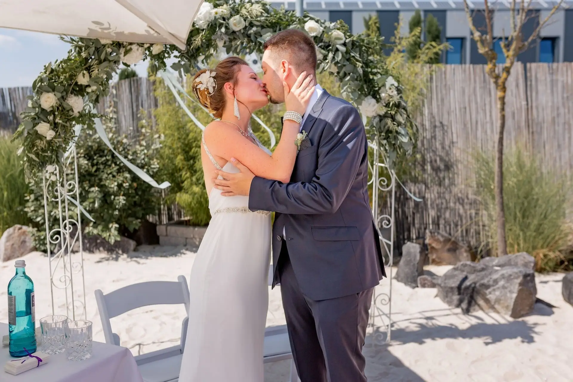 Der erste Kuss als Ehepaar: Brautpaar küsst sich leidenschaftlich unter der Markise auf dem Sandstrand des Miio