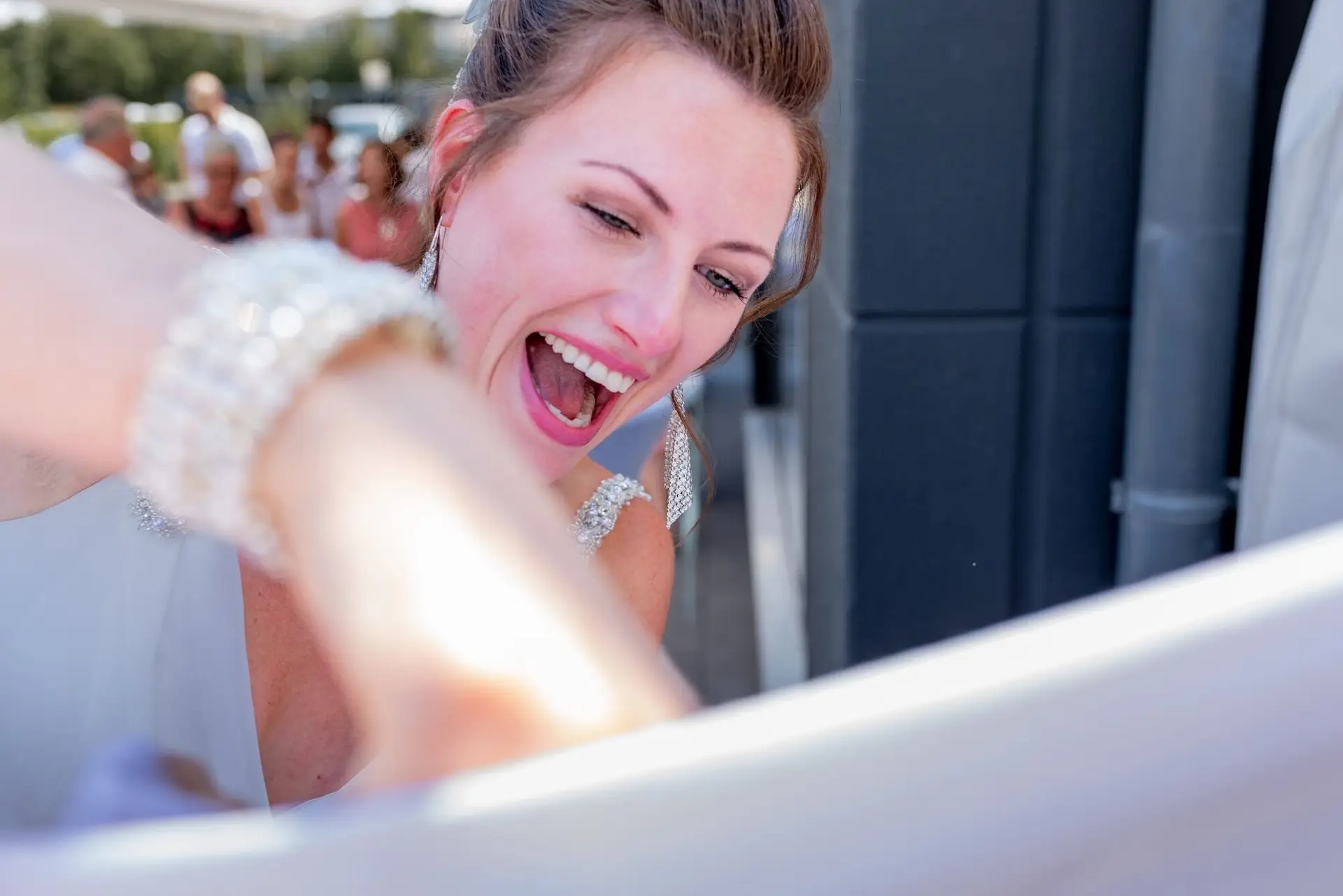 Bräutigam schreibt auf das große weiße Hochzeitsbanner, Braut schaut lächelnd durch einen Spiegel auf das Fest