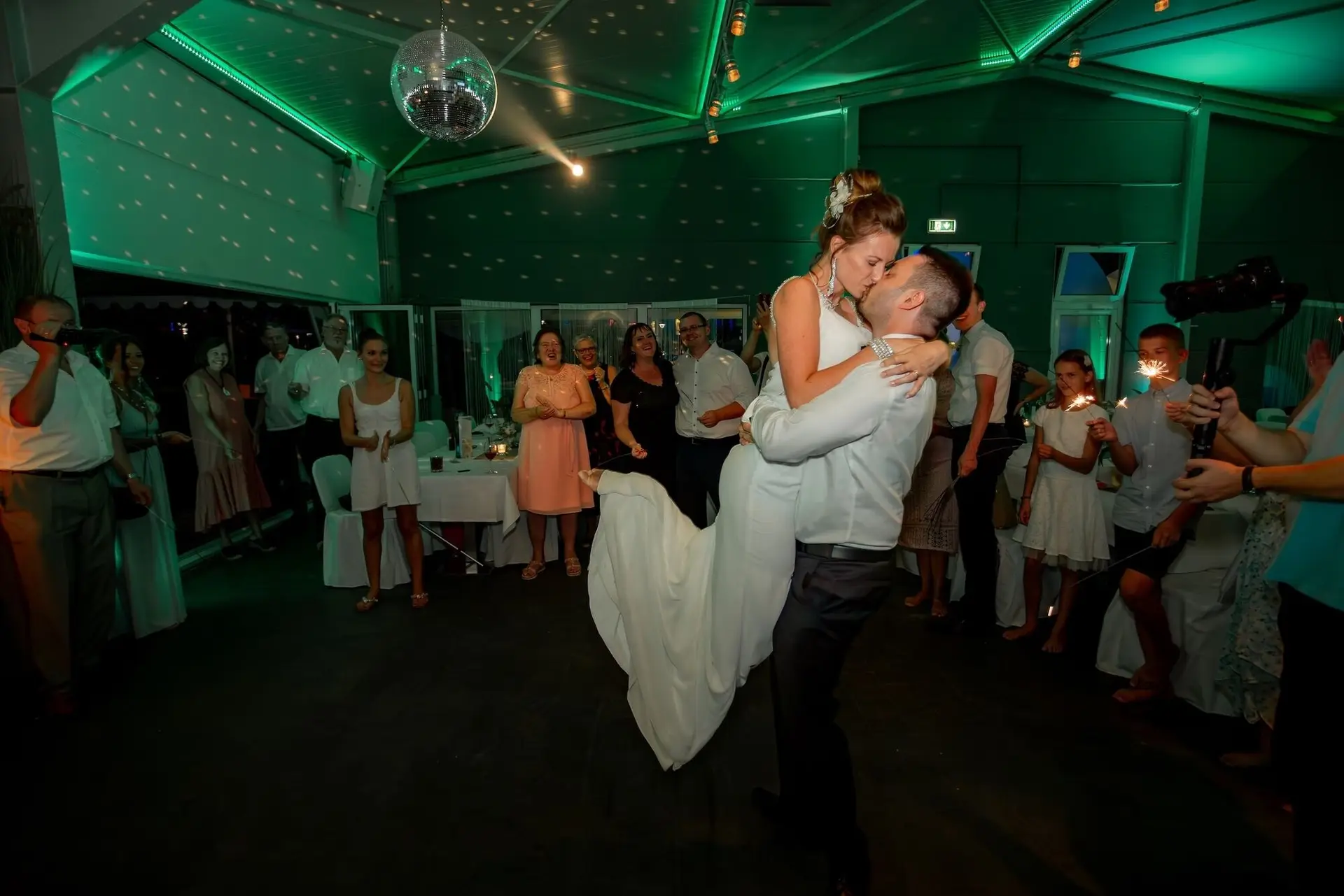 Bräutigam hebt seine Braut jubelnd in die Luft beim Tanz, Gäste ringsum mit Wunderkerzen