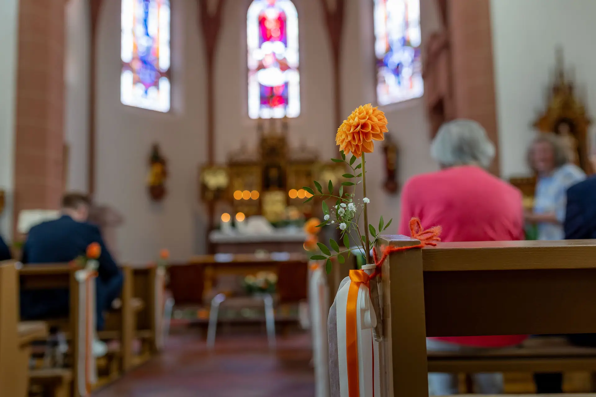 Orangefarbene Blume in Glasvase dekoriert eine Kirchenbank in St. Johannes der Täufer Bad Münster