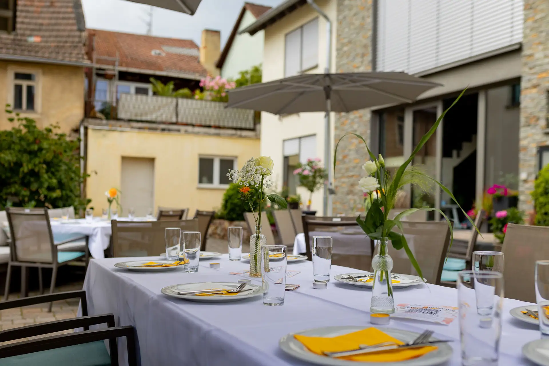 Festlich gedeckter Tisch mit Blumendekoration und Sonnenschirm im Garten des Wallhäuser Weintreffs