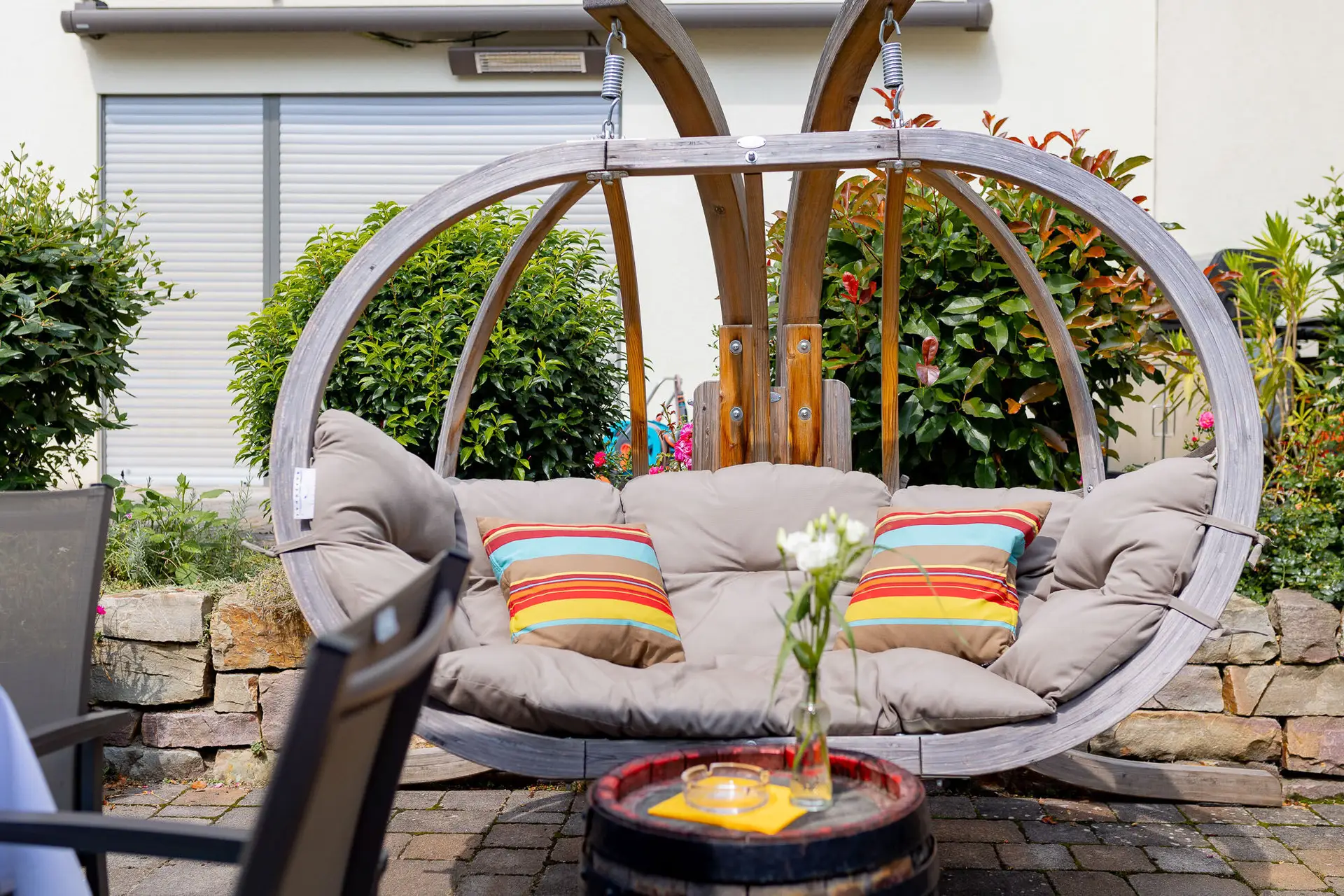 Jana Julian Haengesessel Bunte Kissen Garten Weintreff.PI6O CS6 Hängesessel mit bunten Kissen und Blumenvase im Garten des Wallhäuser Weintreffs