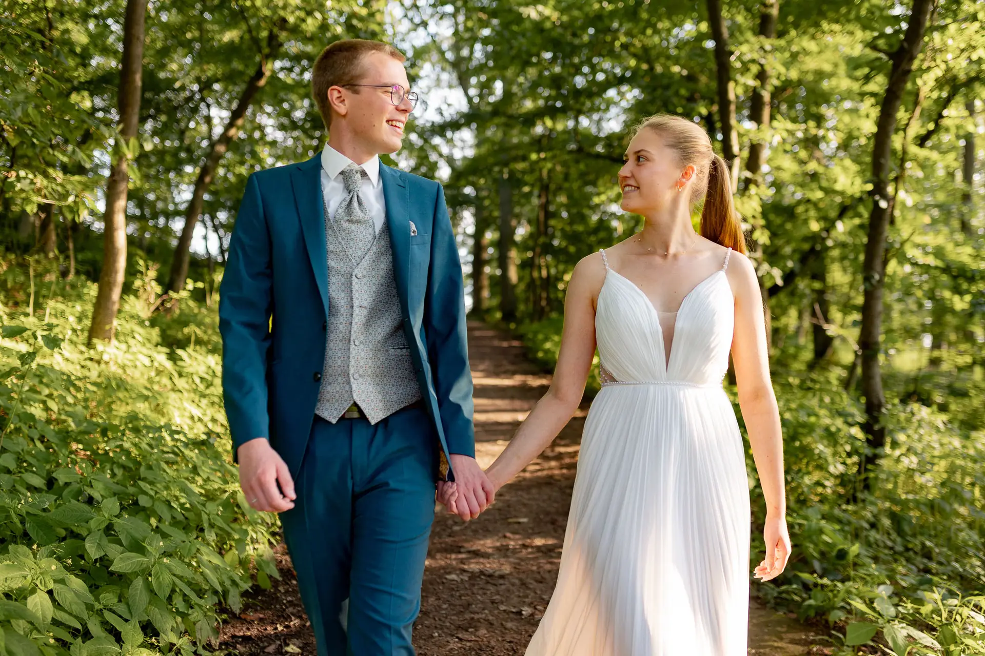 Brautpaar läuft Hand in Hand durch sommerlichen Wald bei Burg Ebernburg