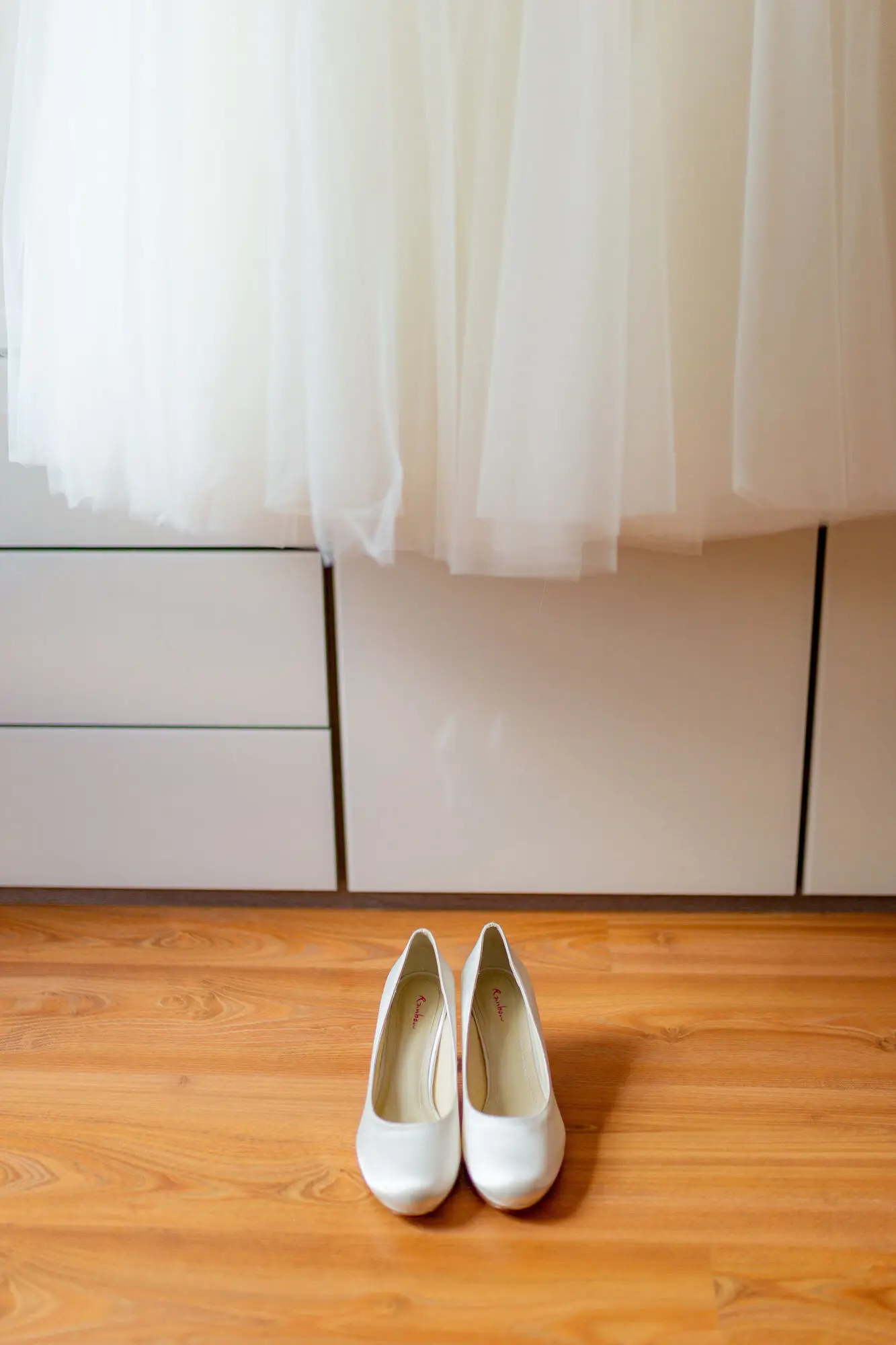 Weiße Brautschuhe vor dem hängenden Brautkleid