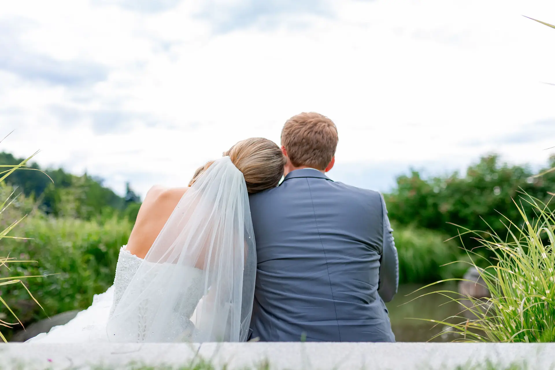 Brautpaar sitzt eng aneinander auf einer Bank, Rückansicht mit Bergpanorama