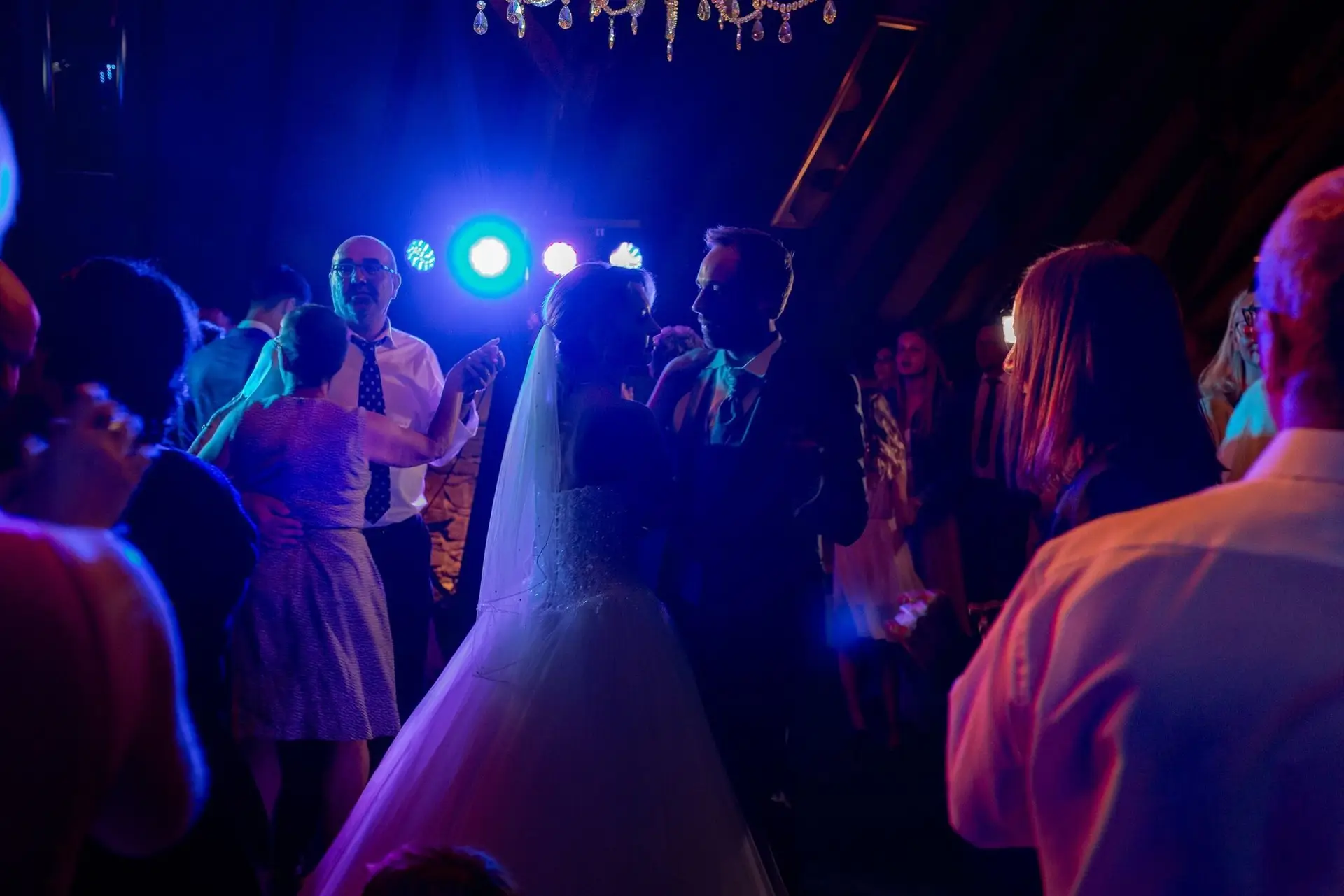 Braut tanzt mit Gästen unter buntem Partylicht in der Scheune des Hofgut Hohenstein