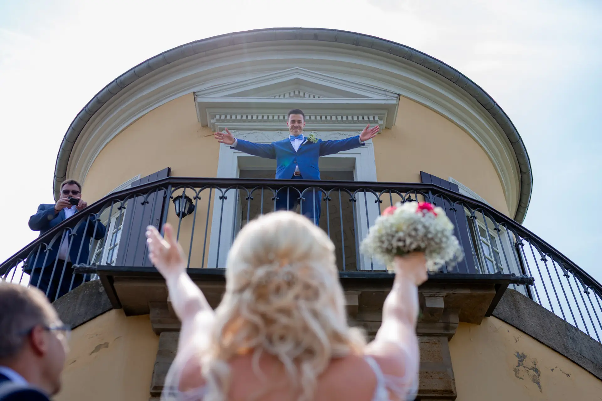 Kevin breitet die Arme auf dem Balkon aus, Liane schaut von unten zu ihm hoch – erster Blick am Schlosspavillon