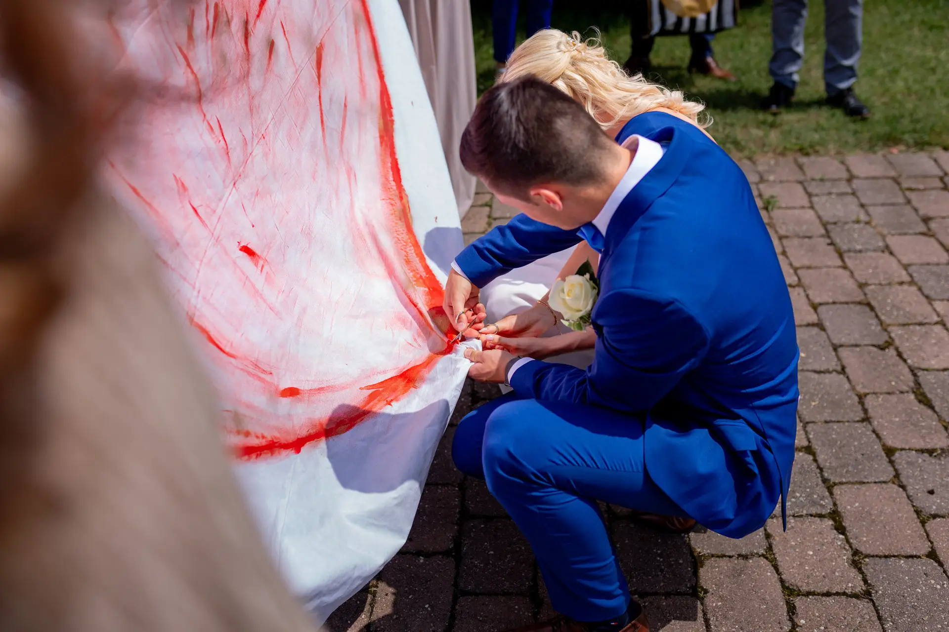 Liane und Kevin schneiden gemeinsam ein Herz aus einem Tuch – Hochzeitsspiel am Schlosspavillon