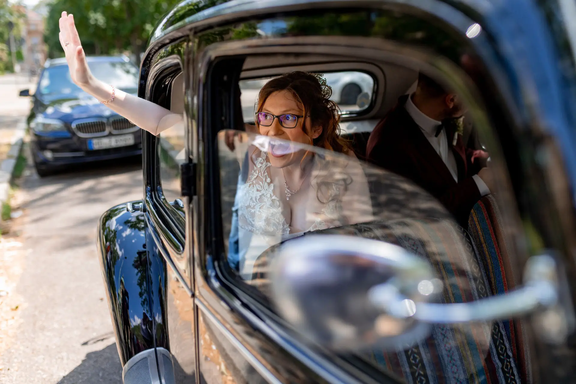 Mirjam winkt mit Brille aus dem dunklen Oldtimer nach der Trauung in der Christuskirche Mannheim
