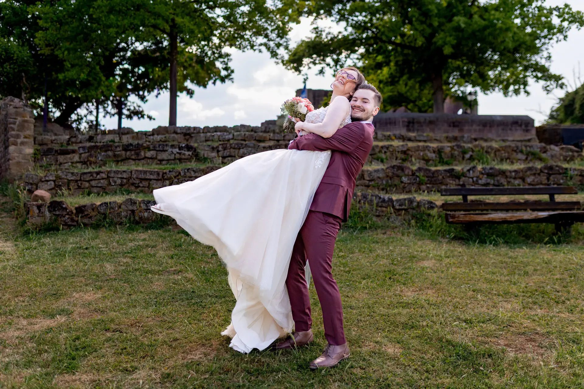 Bräutigam hebt seine Braut schwungvoll in die Luft vor der Bruchsteinmauer der Burg Neuleiningen
