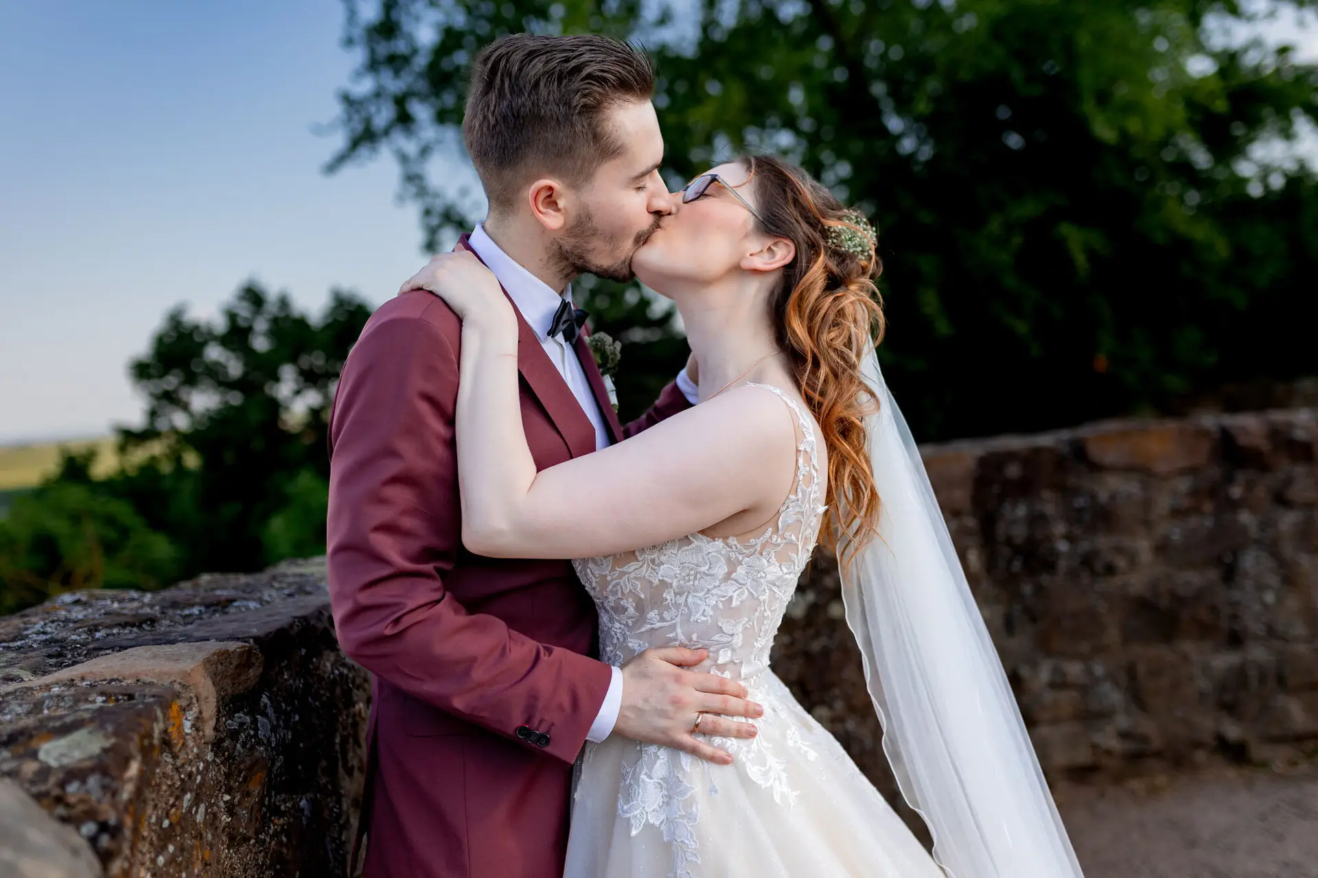 Brautpaar küsst sich unter dem grasbewachsenen Burghügel, romantische Stimmung im Außenbereich der Burg