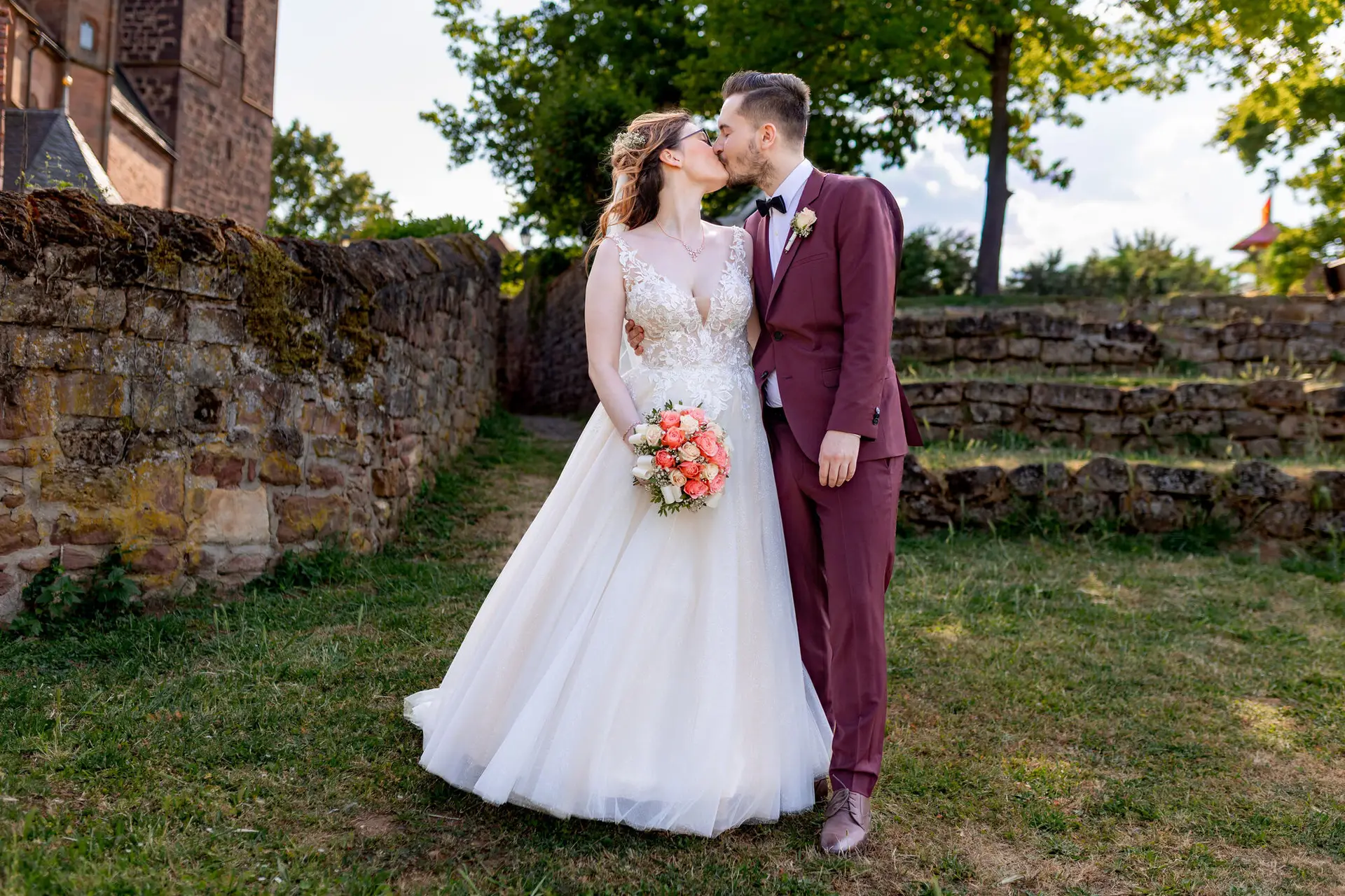 Braut und Bräutigam küssen sich innig vor dem moosbewachsenen Mauerwerk der Burg Neuleiningen