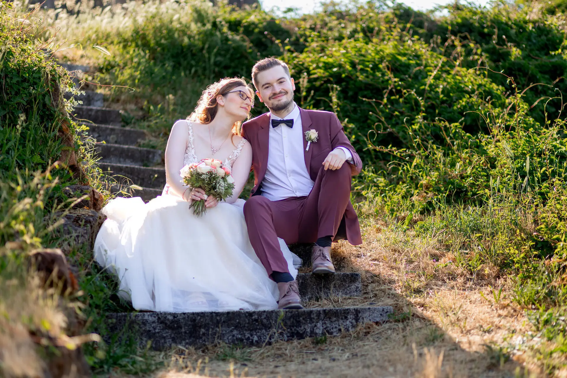 Brautpaar sitzt auf einer alten Steintreppe der Burganlage und schaut sich liebevoll an, umgeben von Grün