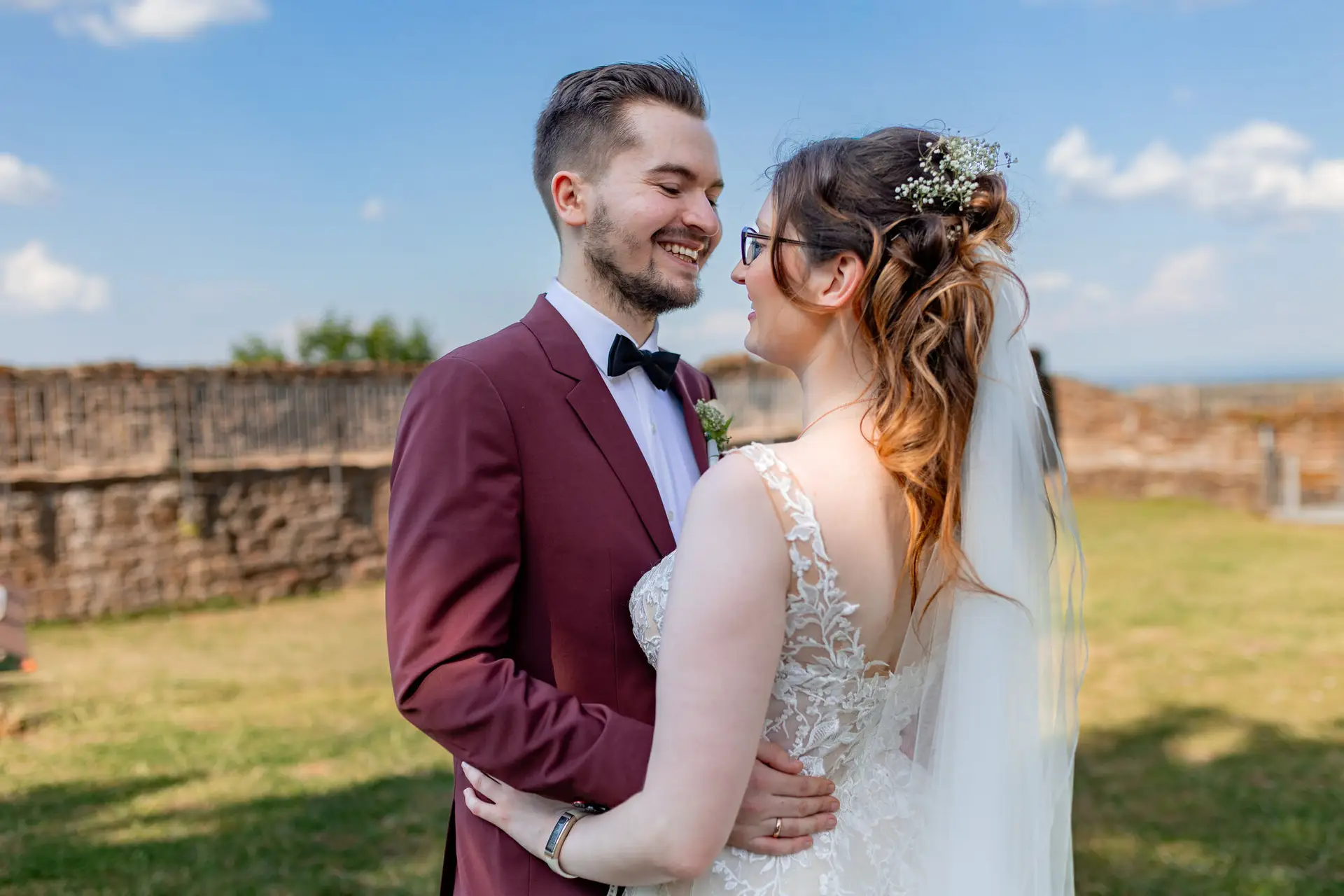 Brautpaar lächelt sich glücklich vor dem mittelalterlichen Steinwall der Burg Neuleiningen bei blauem Himmel an