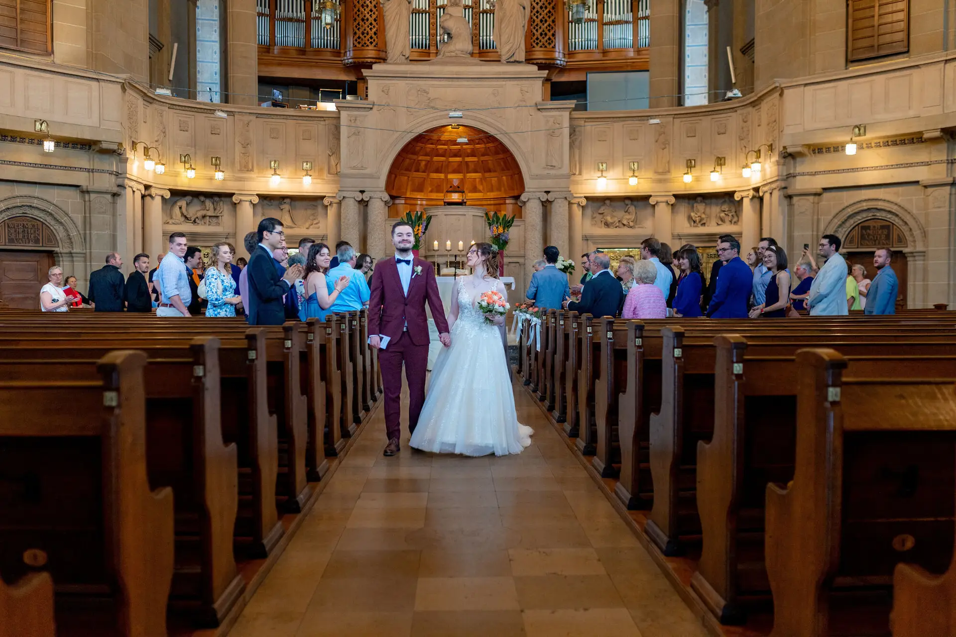 Brautpaar schreitet durch den gotischen Kirchenraum, umgeben von Gästen nach der Trauung