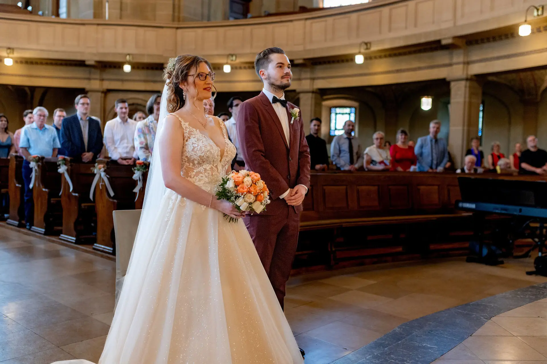 Braut und Bräutigam stehen würdevoll vor dem Kirchenaltar mit Gästen auf beiden Seiten
