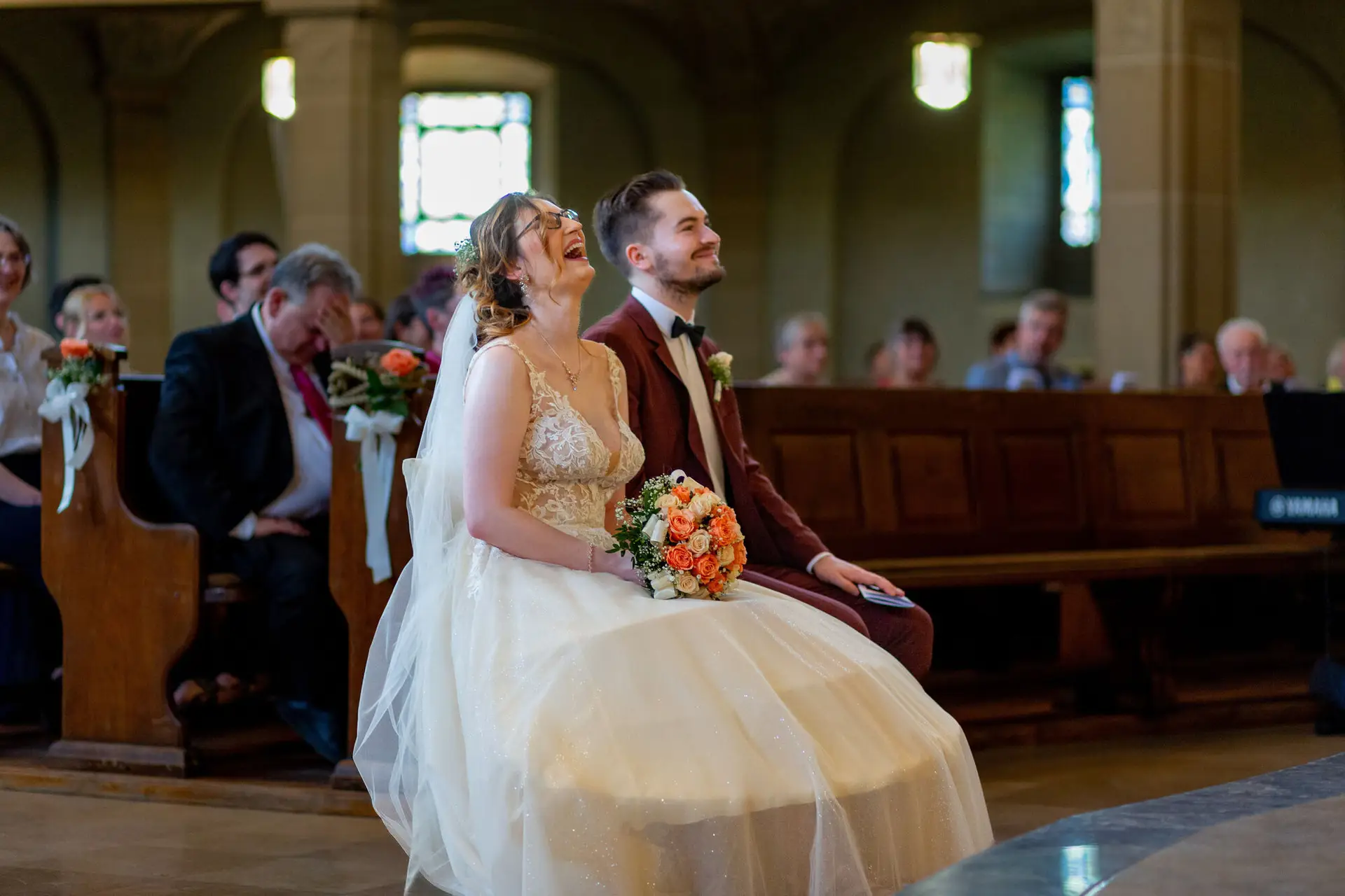 Braut und Bräutigam sitzen glücklich nebeneinander im Kirchenschiff während der Trauung