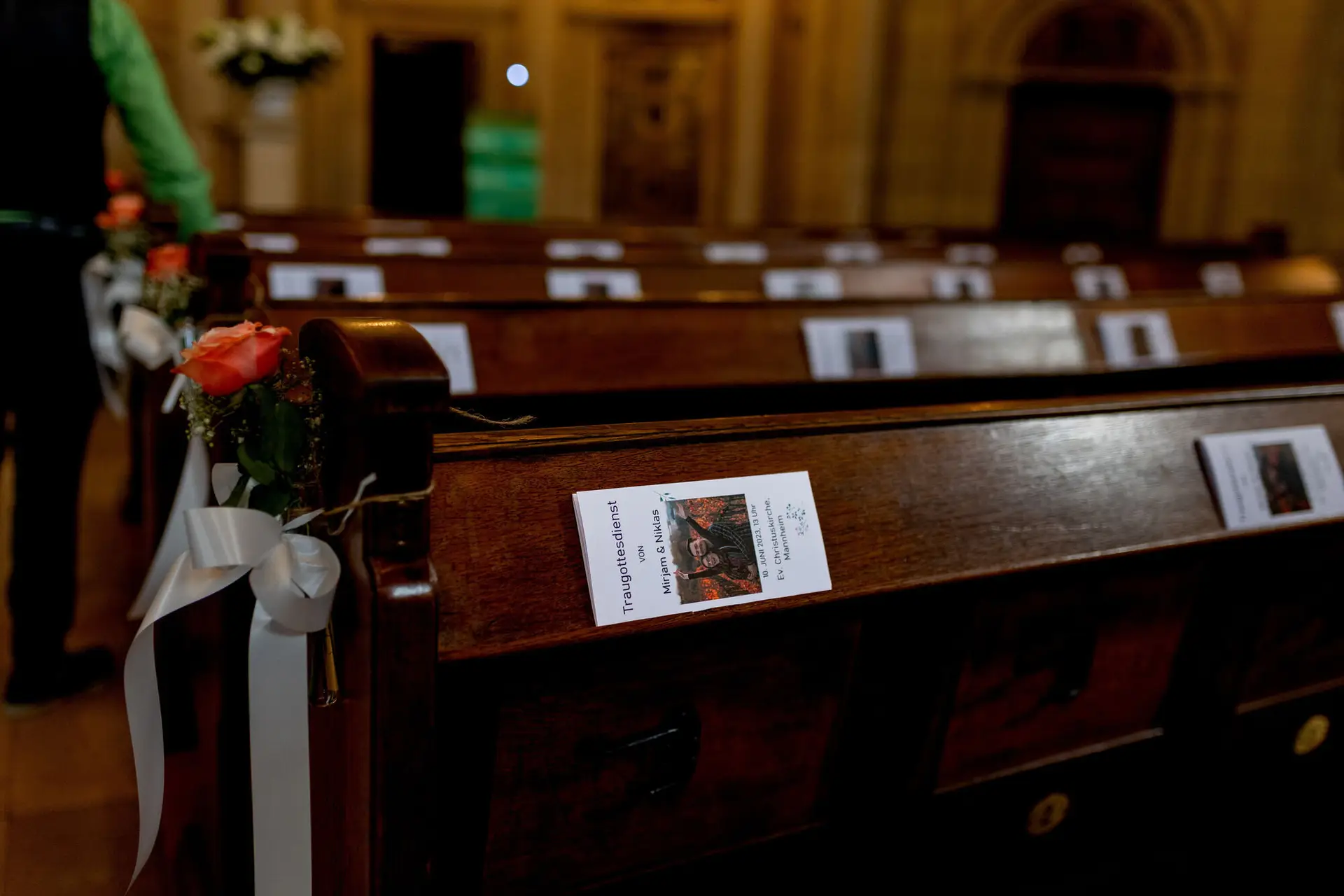 Geschmückte Kirchenbänke mit Programmheften und rosa Rosen in der Christuskirche Mannheim vor der Trauung