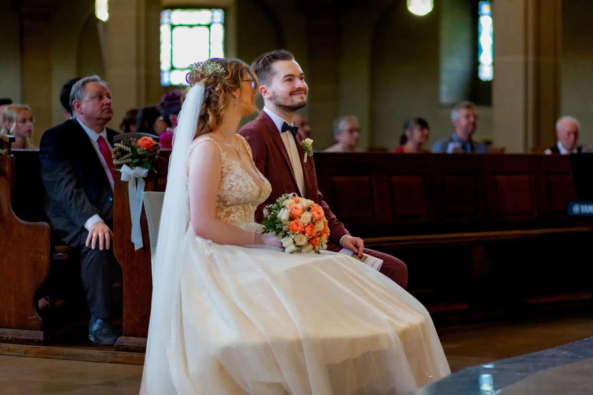 Brautpaar sitzt in der Kirchenbank der Christuskirche Mannheim während der Trauung, orangefarbener Strauß