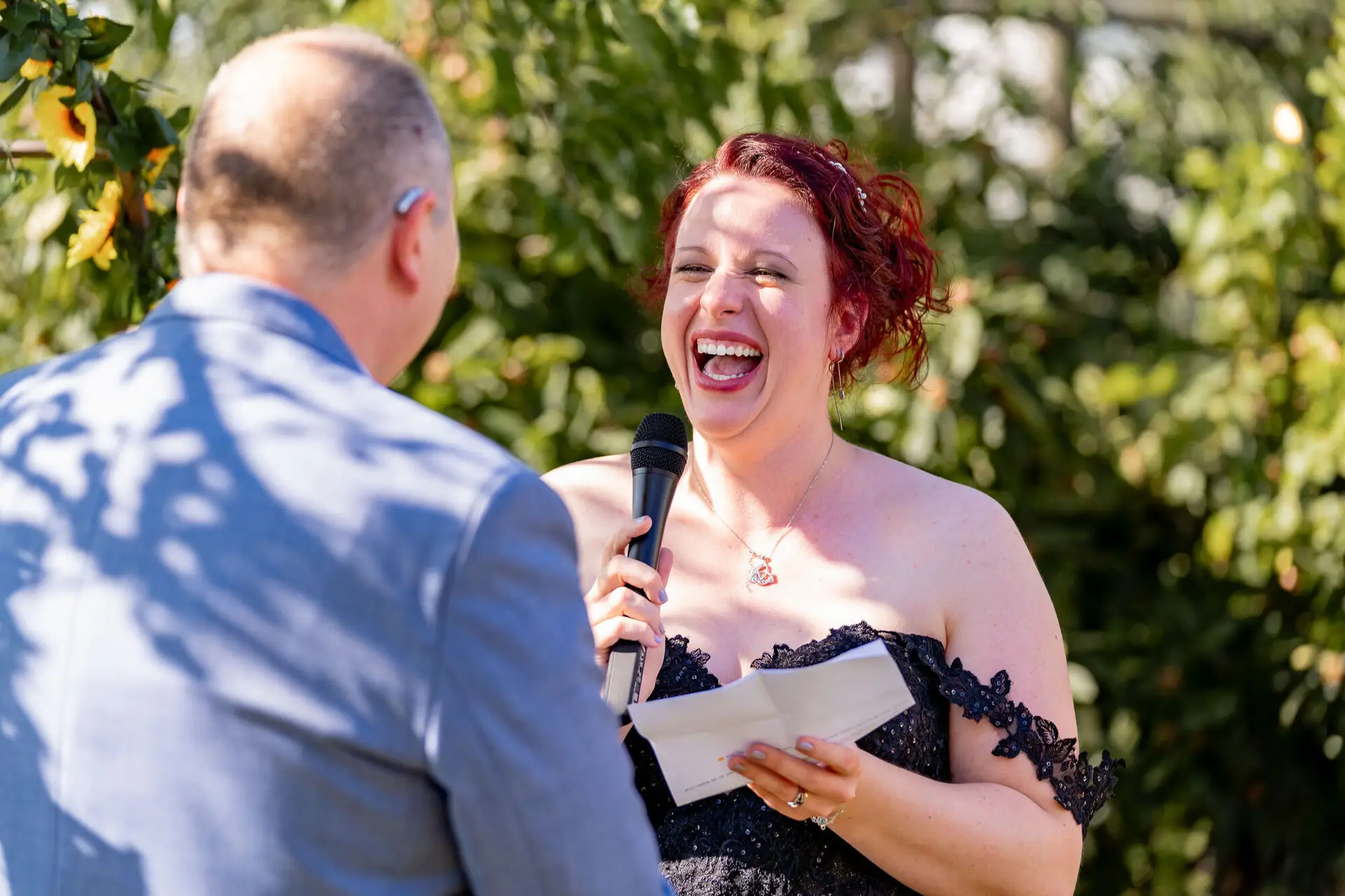 Braut lacht herzlich während sie ihr Eheversprechen mit Mikrofon vorträgt