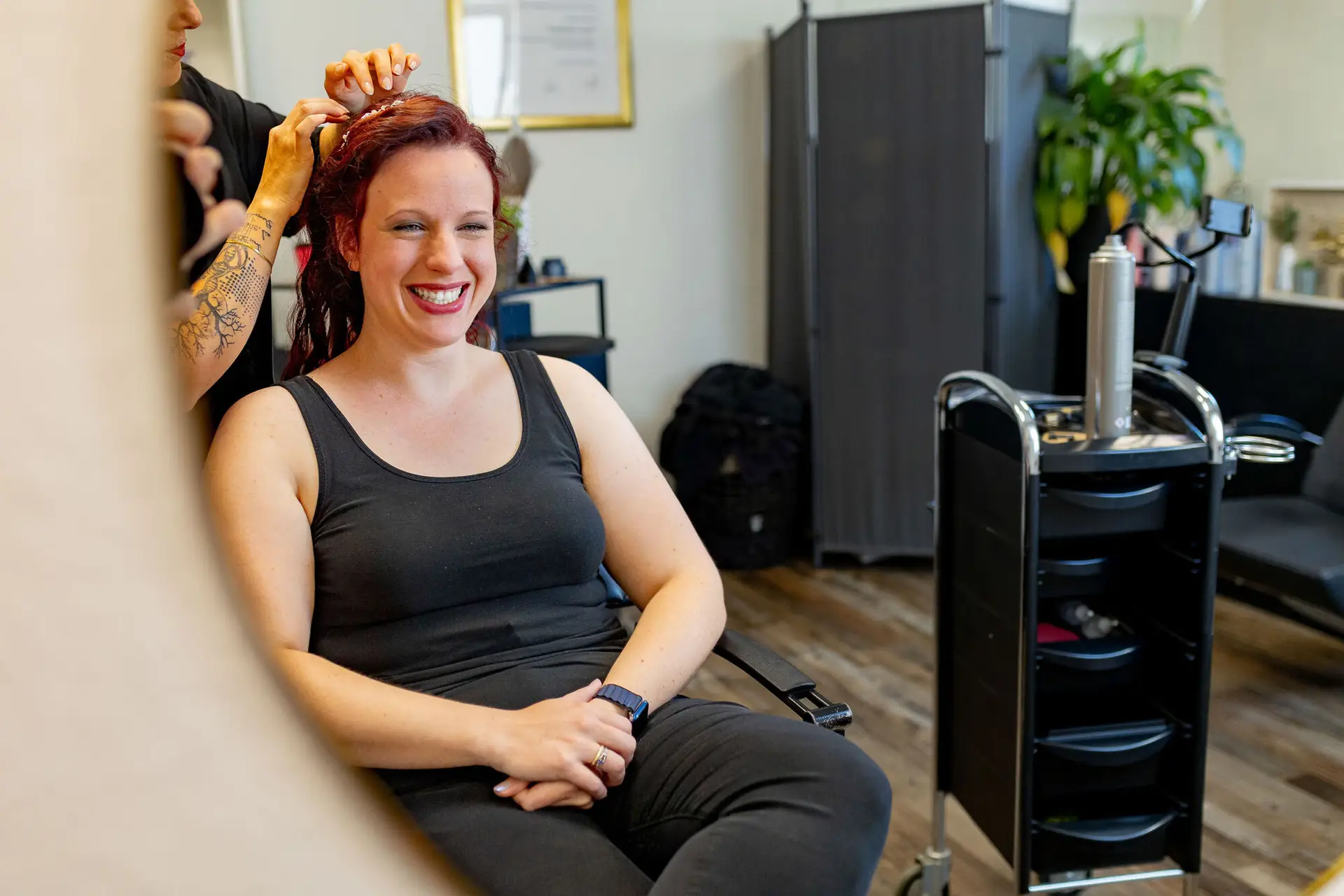 Strahlende Braut lächelt während Friseurin Hochzeitsfrisur stylt