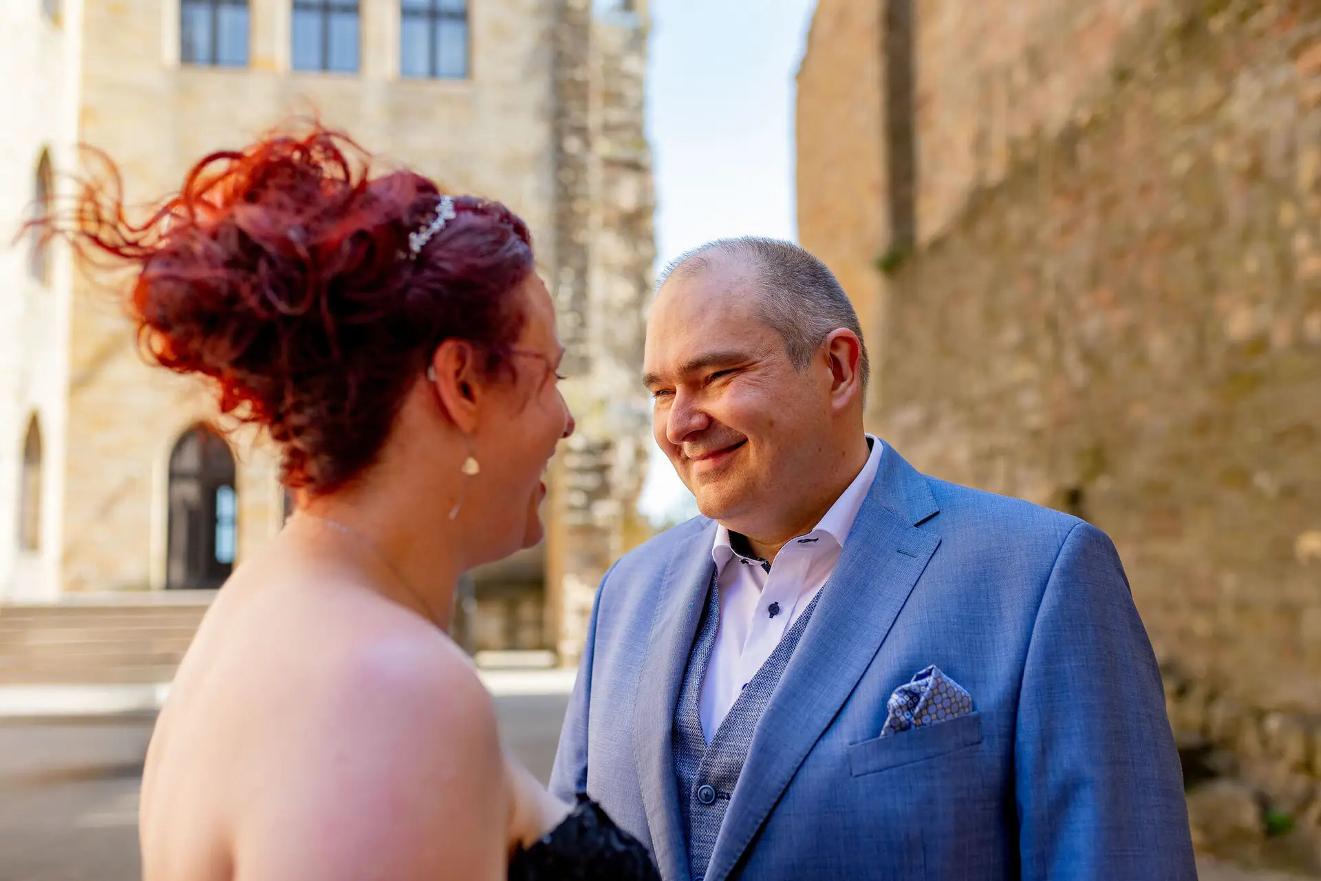 Brautpaar lacht sich glücklich an während Wind durch rote Haare der Braut weht