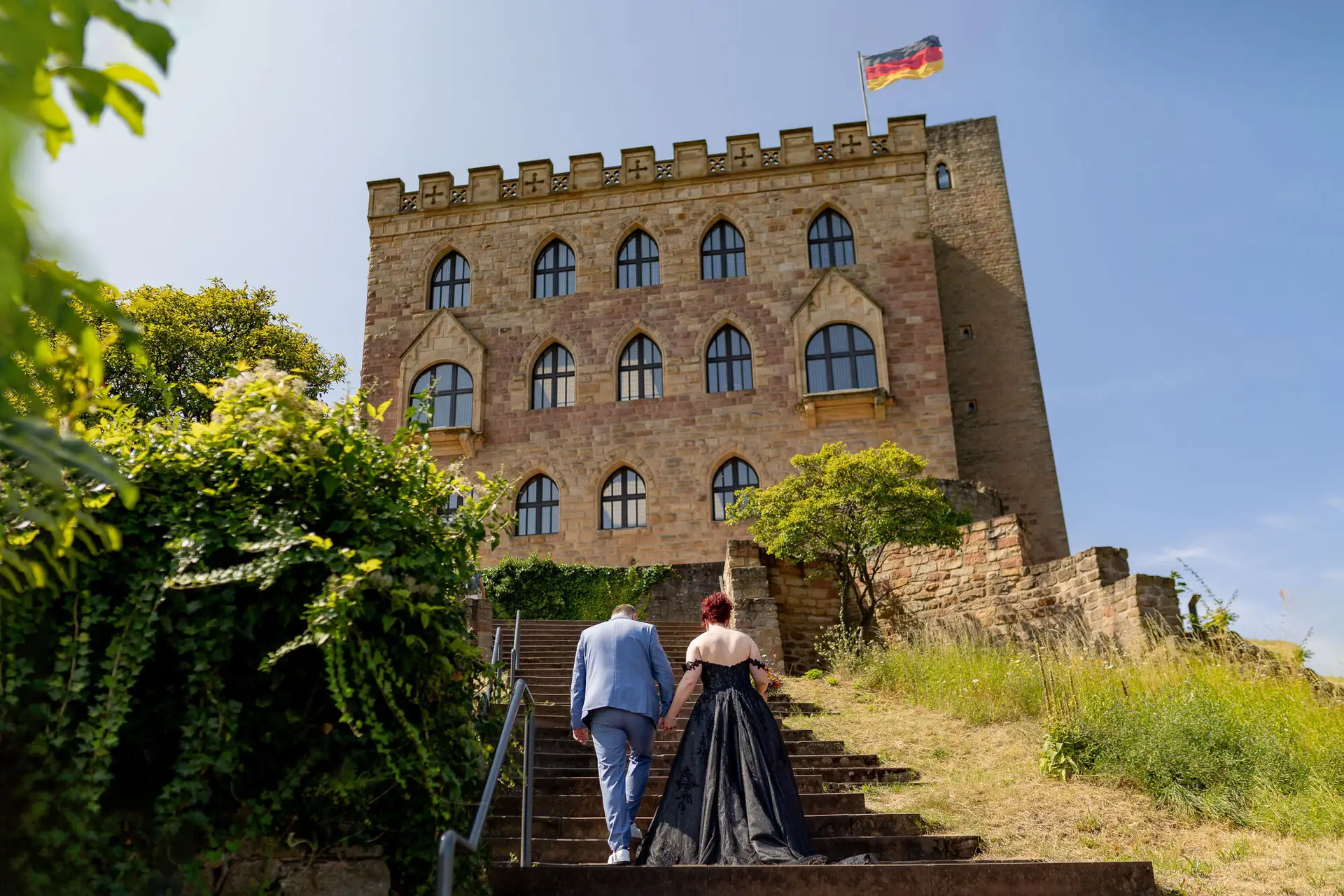 Brautpaar steigt gemeinsam steinerne Treppe zum Hambacher Schloss hinauf - Rückenansicht