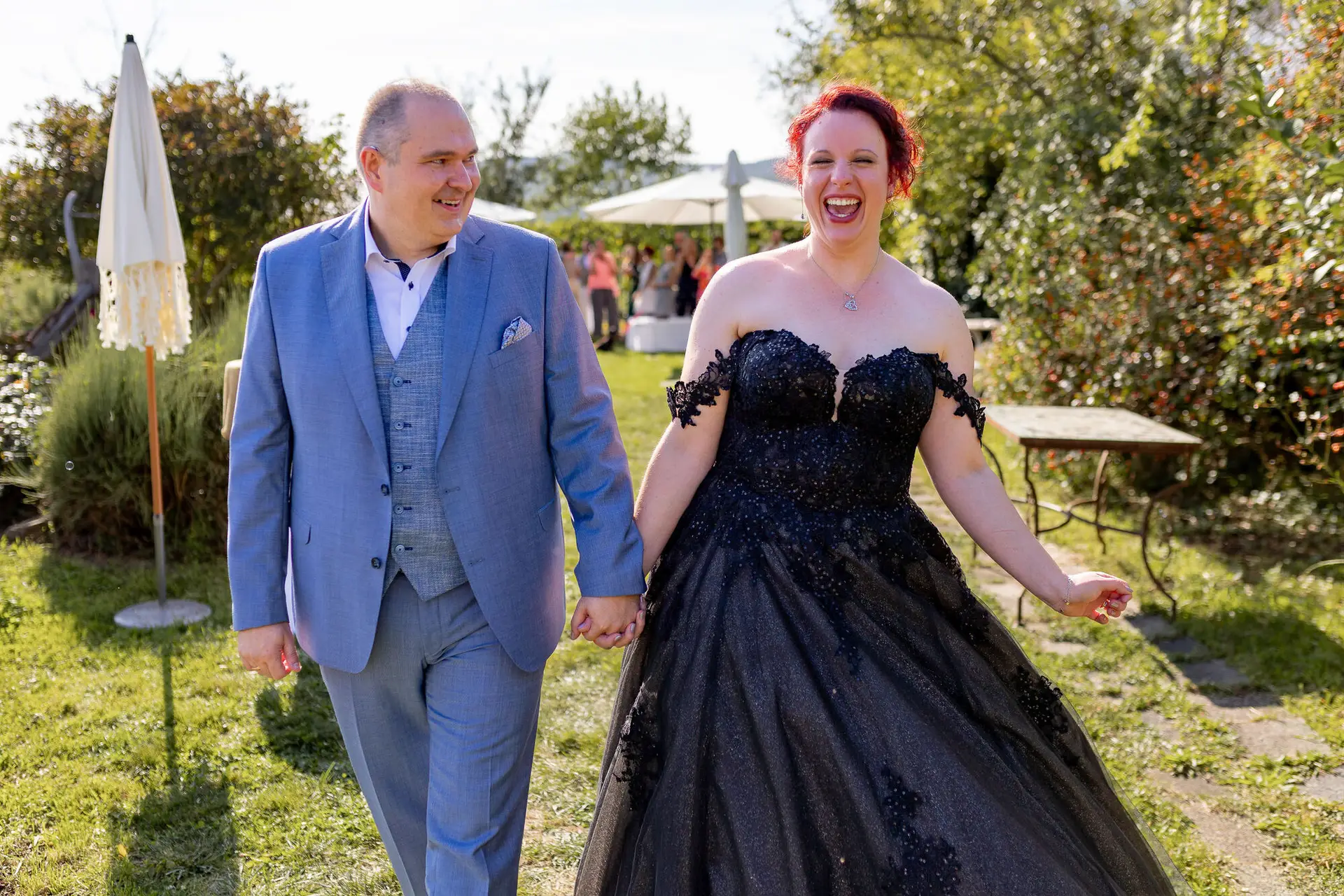 Brautpaar läuft lachend Hand in Hand durch sonnigen Garten