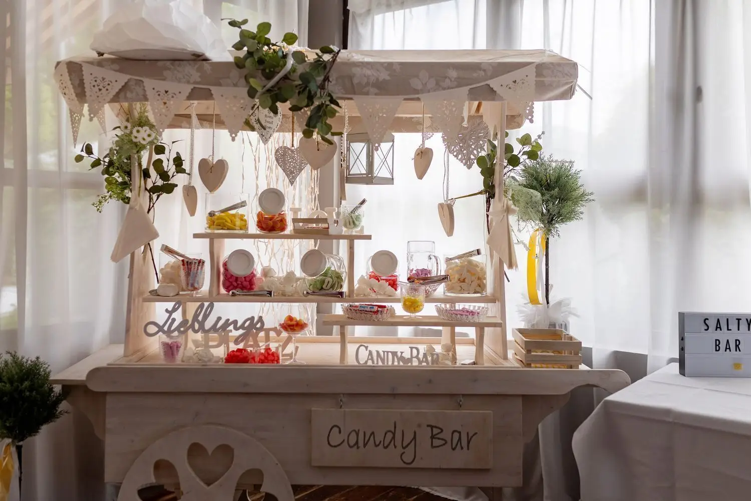 Weißer Candy Bar-Tisch mit bunten Süßigkeiten, Zuckerstangen und liebevoller Hochzeitsdekoration