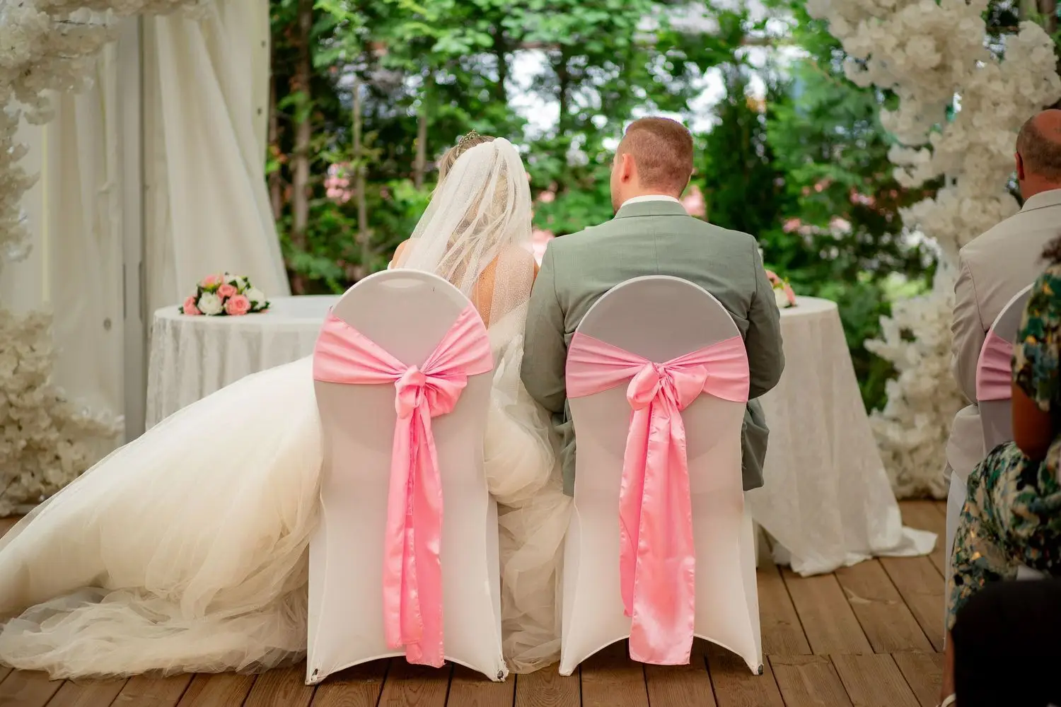 Brautpaar sitzt am Altar mit rosa Schleifen an den Stühlen, Rückansicht bei der freien Trauung