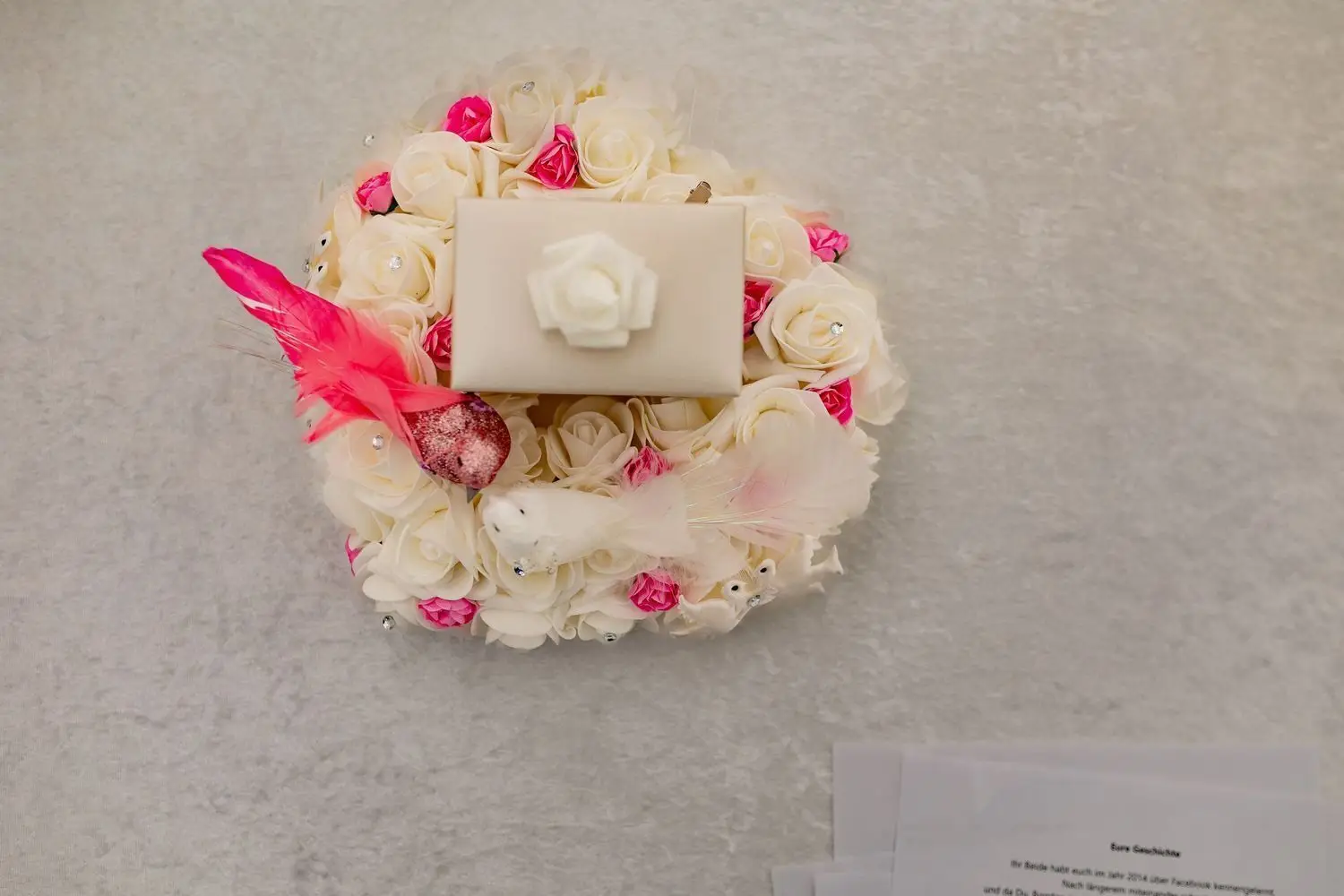 Detailaufnahme des weißen Ringkastens mit weißen Rosen, Kristallen und einer roten Feder