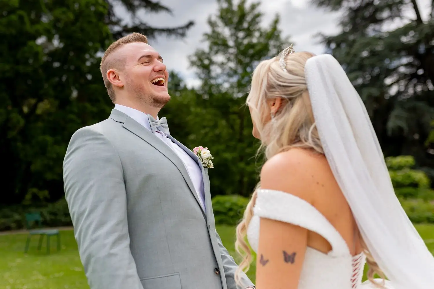Bräutigam lacht herzlich in die Kamera, Braut mit langen blonden Haaren und Schleier neben ihm