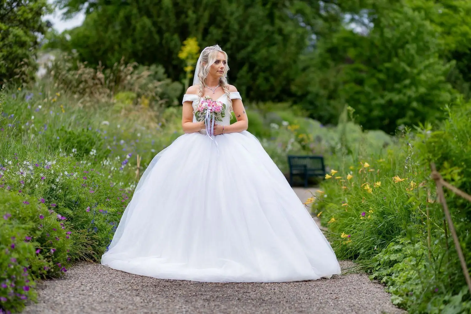Braut in weißem Ballkleid mit Schleier steht allein auf gepflastertem Gartenweg im Hermannshof Weinheim