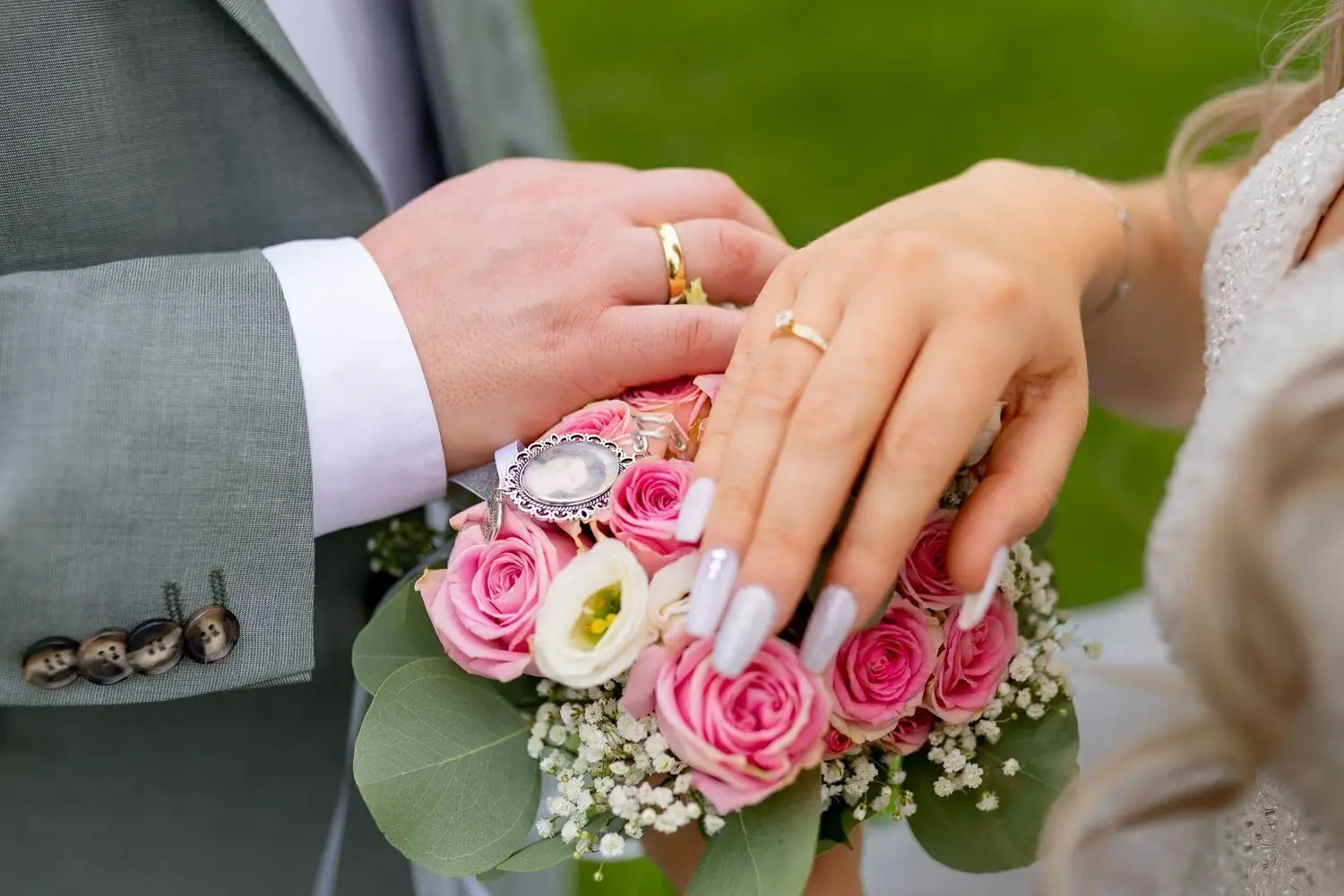 Nahaufnahme der verschränkten Hände des Brautpaares mit goldenen Eheringen und Blumenstrauß