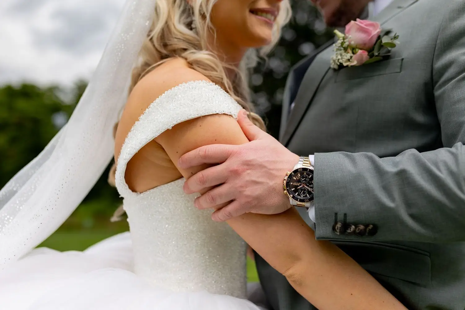 Detailaufnahme – Bräutigams Hand hält zärtlich den Arm der Braut, elegante Uhr am Handgelenk