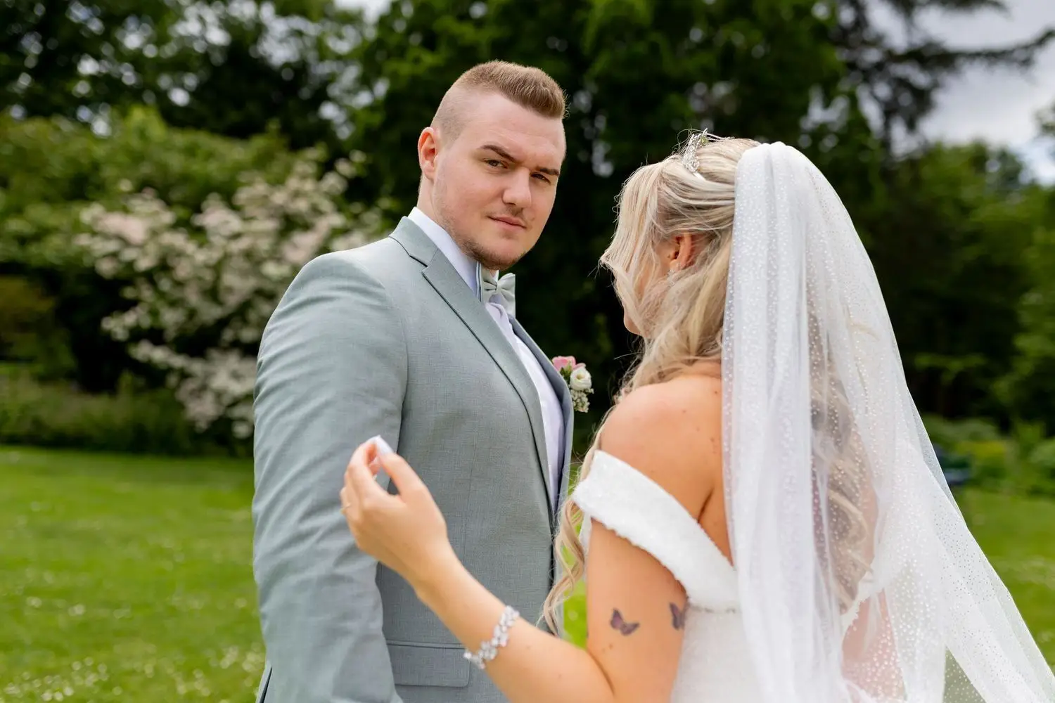 Brautpaar blickt sich ernst und liebevoll an, blühende Bäume im Frühlingsgarten dahinter