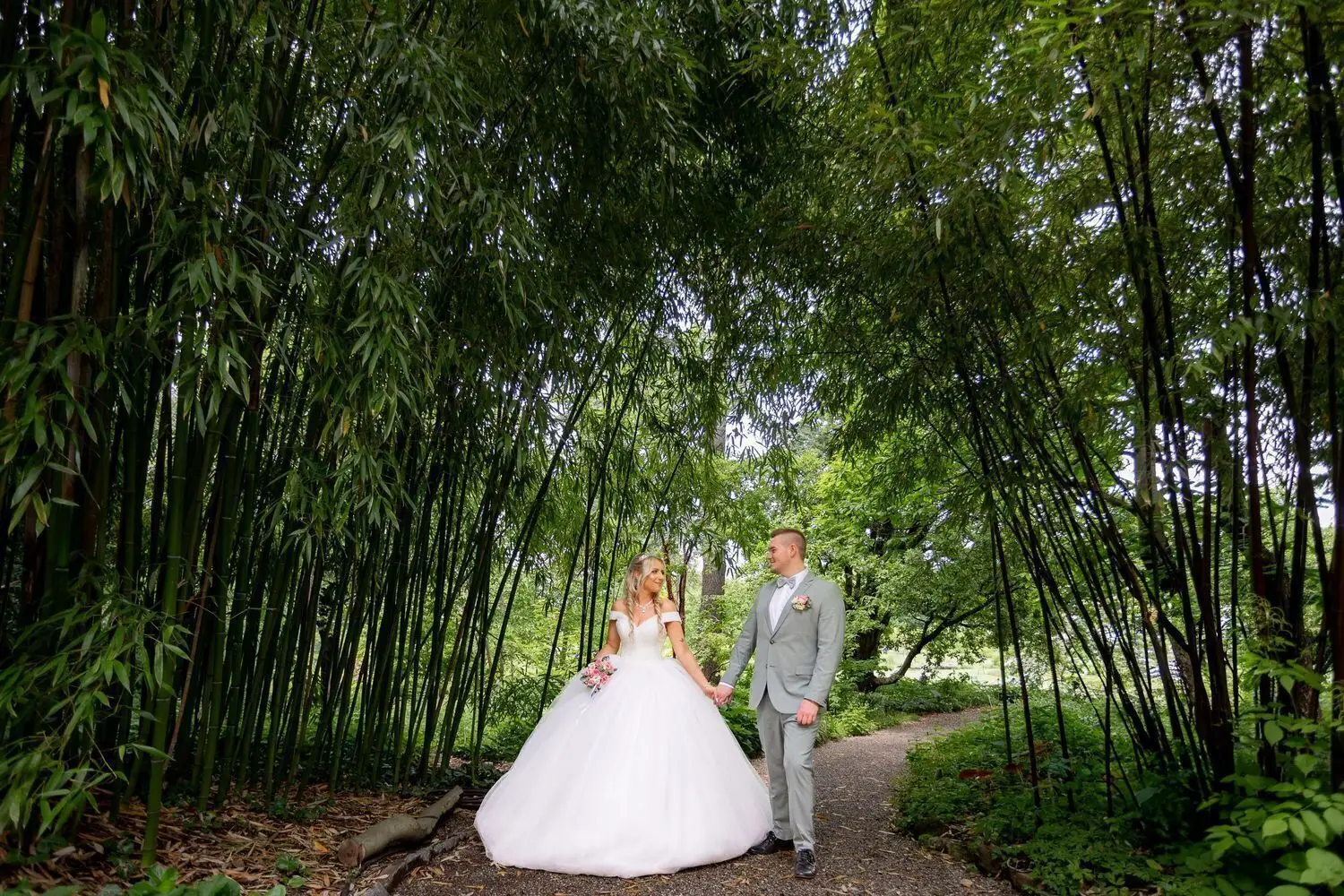 Brautpaar spaziert Hand in Hand auf schmalem Weg zwischen hochgewachsenem Bambus im Hermannshof