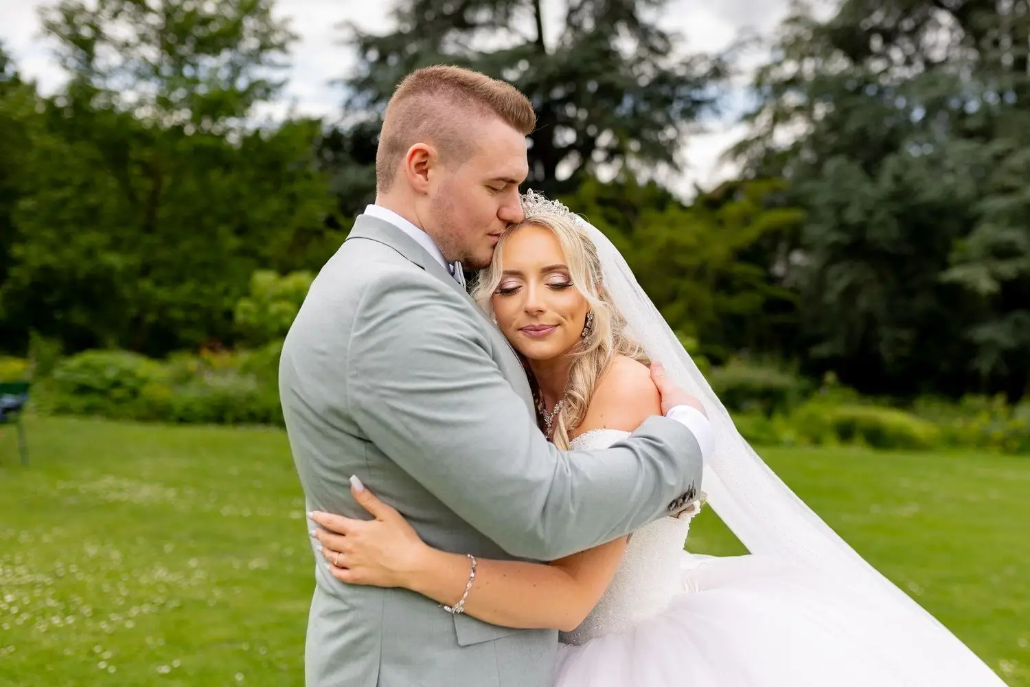 Bräutigam umarmt Braut zärtlich von hinten auf der grünen Wiese des Hermannshof-Gartens