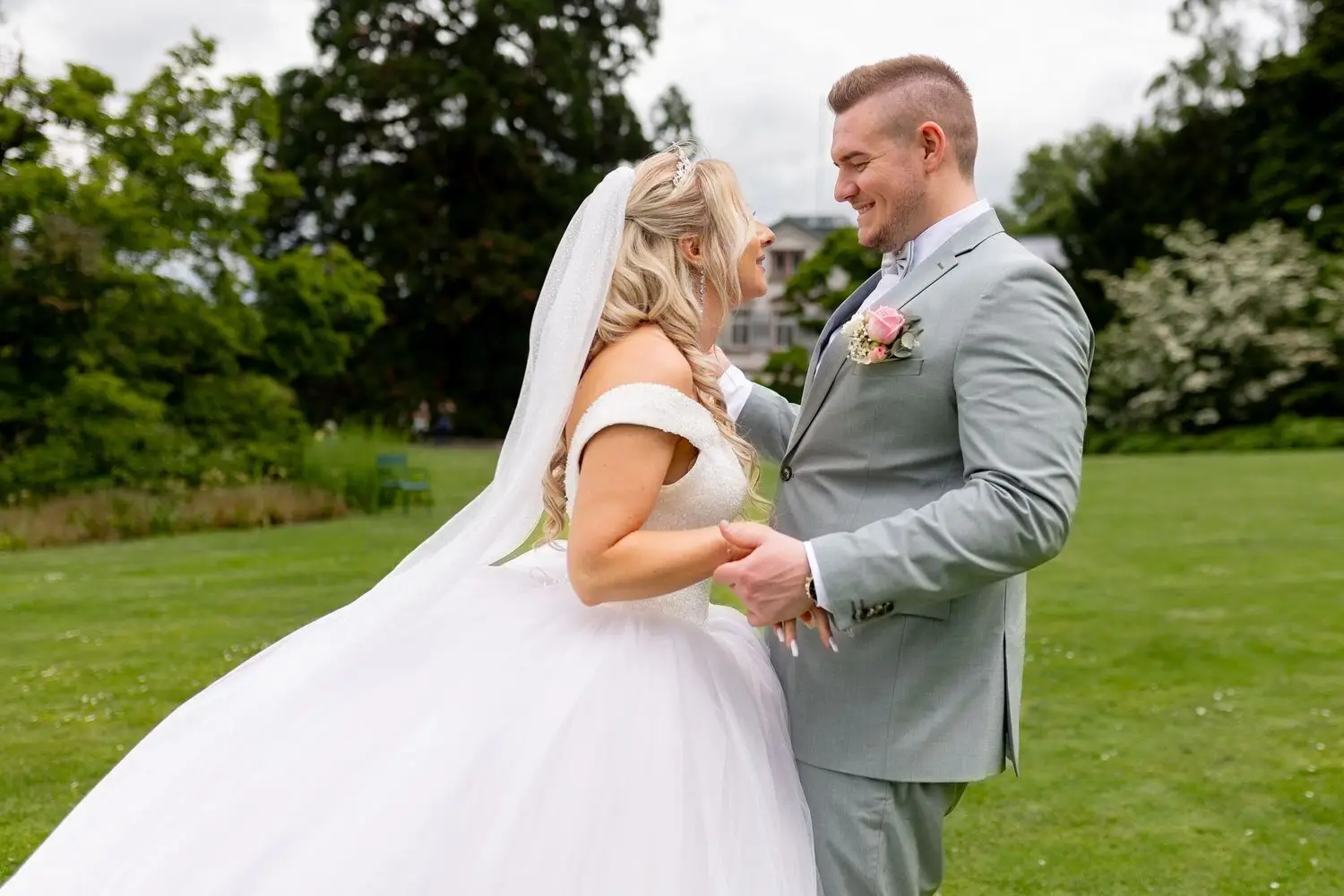 Brautpaar schaut sich verliebt an, elegante Villa und blühender Garten im Hintergrund