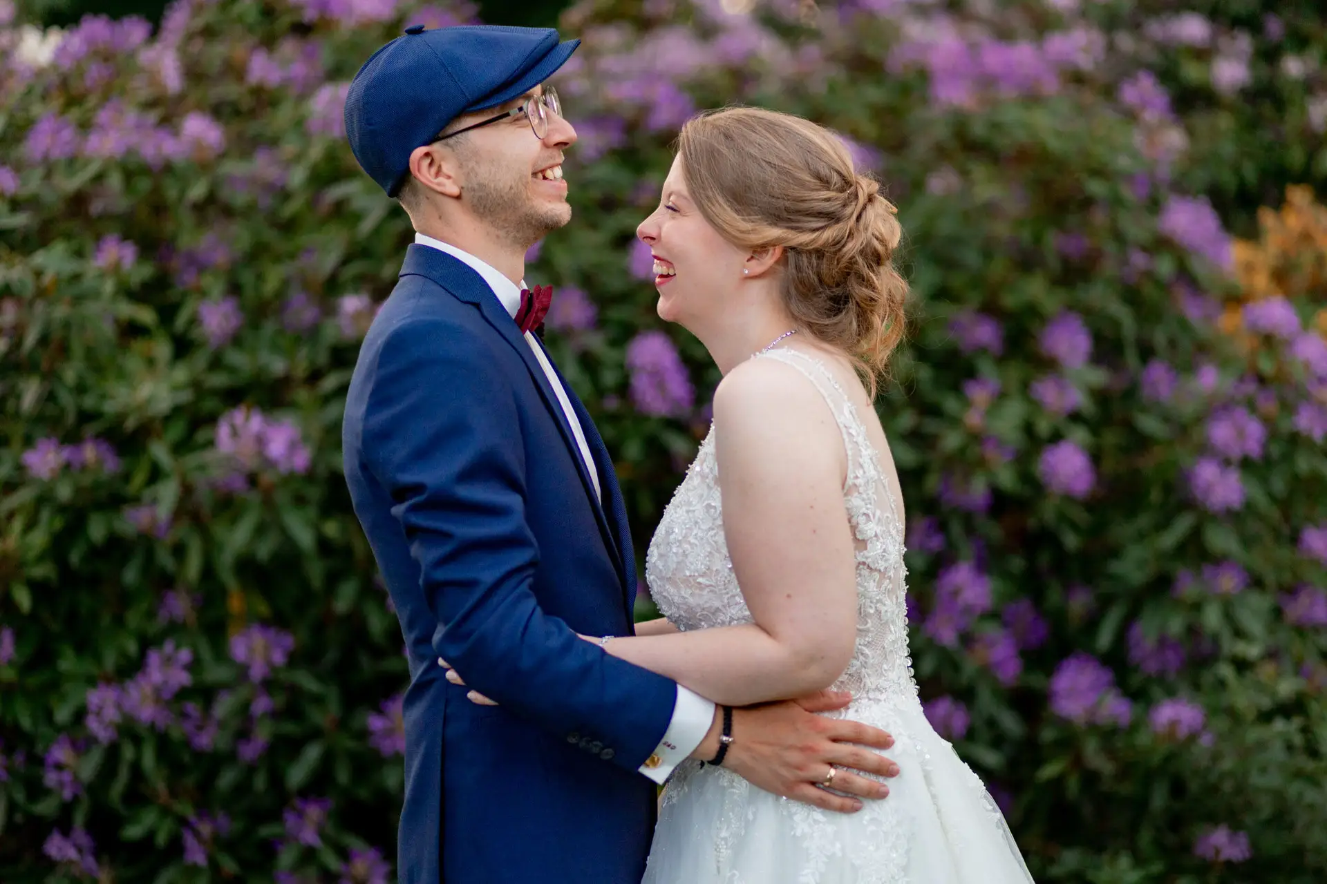 Sandra und Dominic lachen sich an vor lila Rhododendren im Schlosspark Weinheim