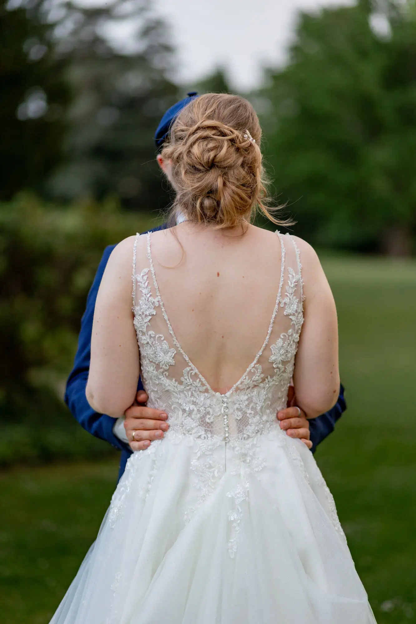 Dominic umarmt Sandra von hinten, Blick auf den Rückenausschnitt des Brautkleids im Schlosspark Weinheim