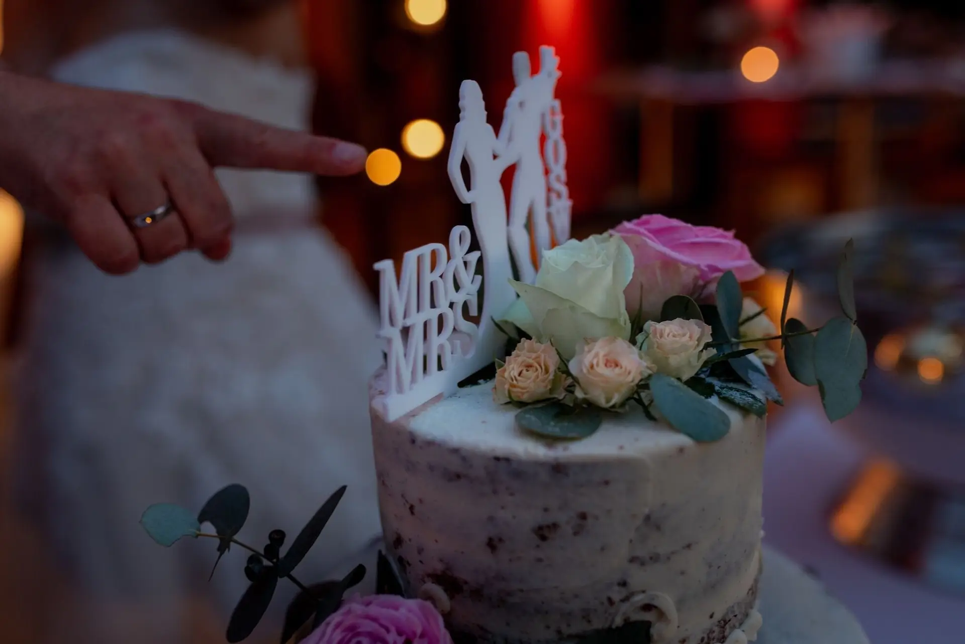 Hochzeitstorte mit "Mr. & Mrs." Aufschrift, Brautpaar zeigt stolz darauf